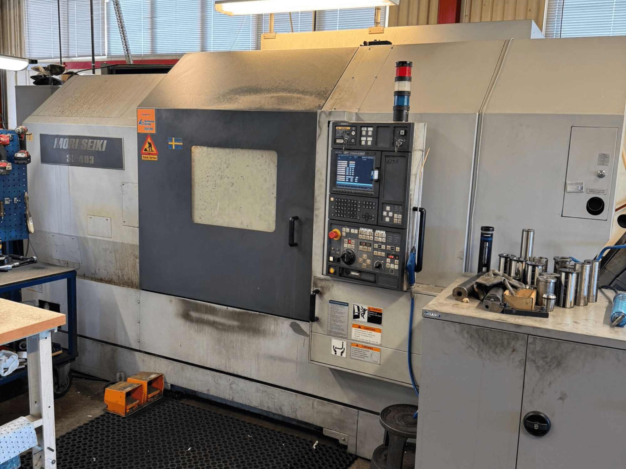 Máquina de torneado horizontal MORI SEIKI SL-403BMC/800 en un taller, mostrando el panel de control y las herramientas cercanas, vista lateral.