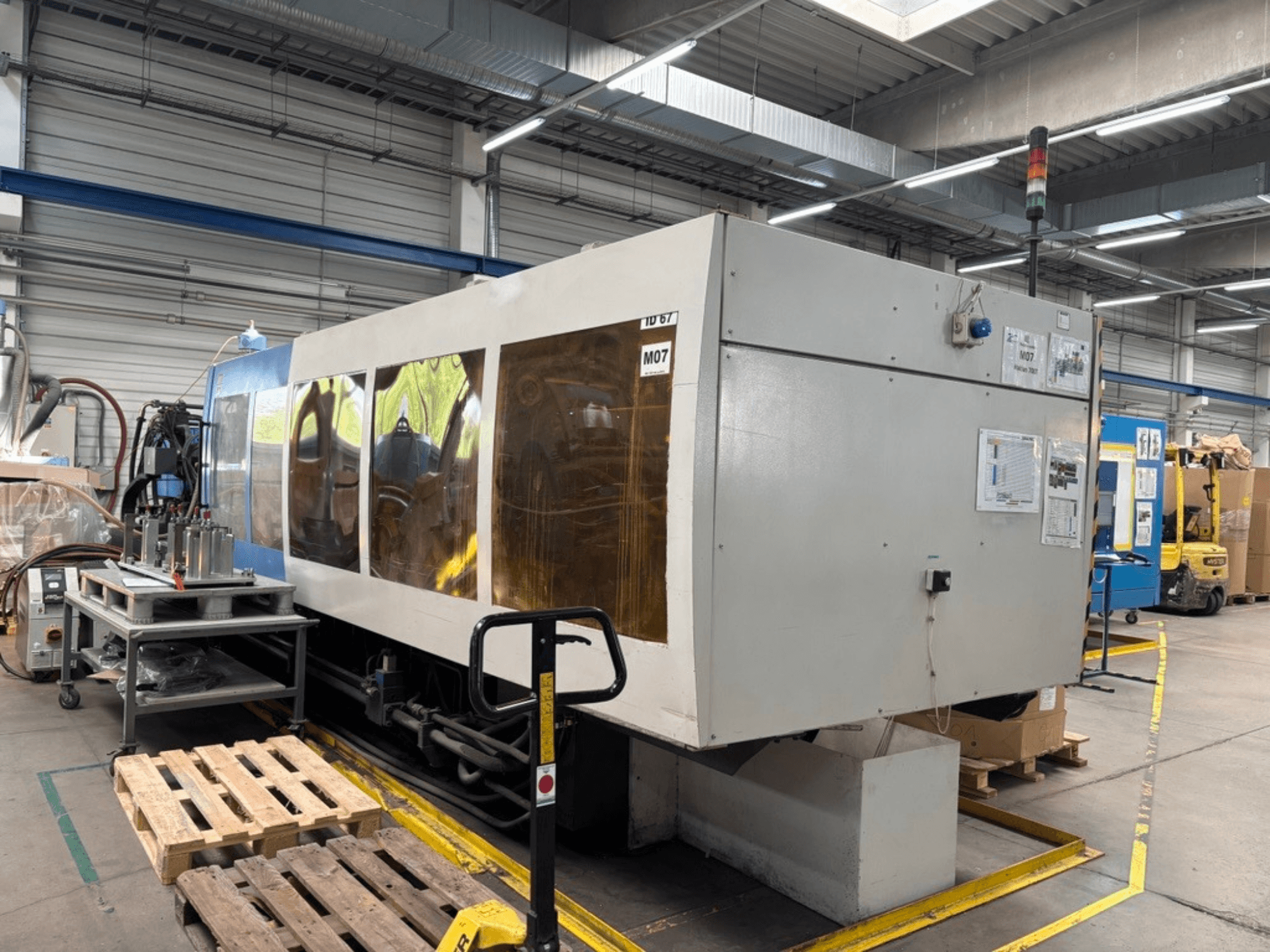 Máquina de moldeo por inyección hidráulica HAITIAN 7000/5000 en una fábrica, vista lateral en la que se aprecian los paneles de control y las luces de seguridad.