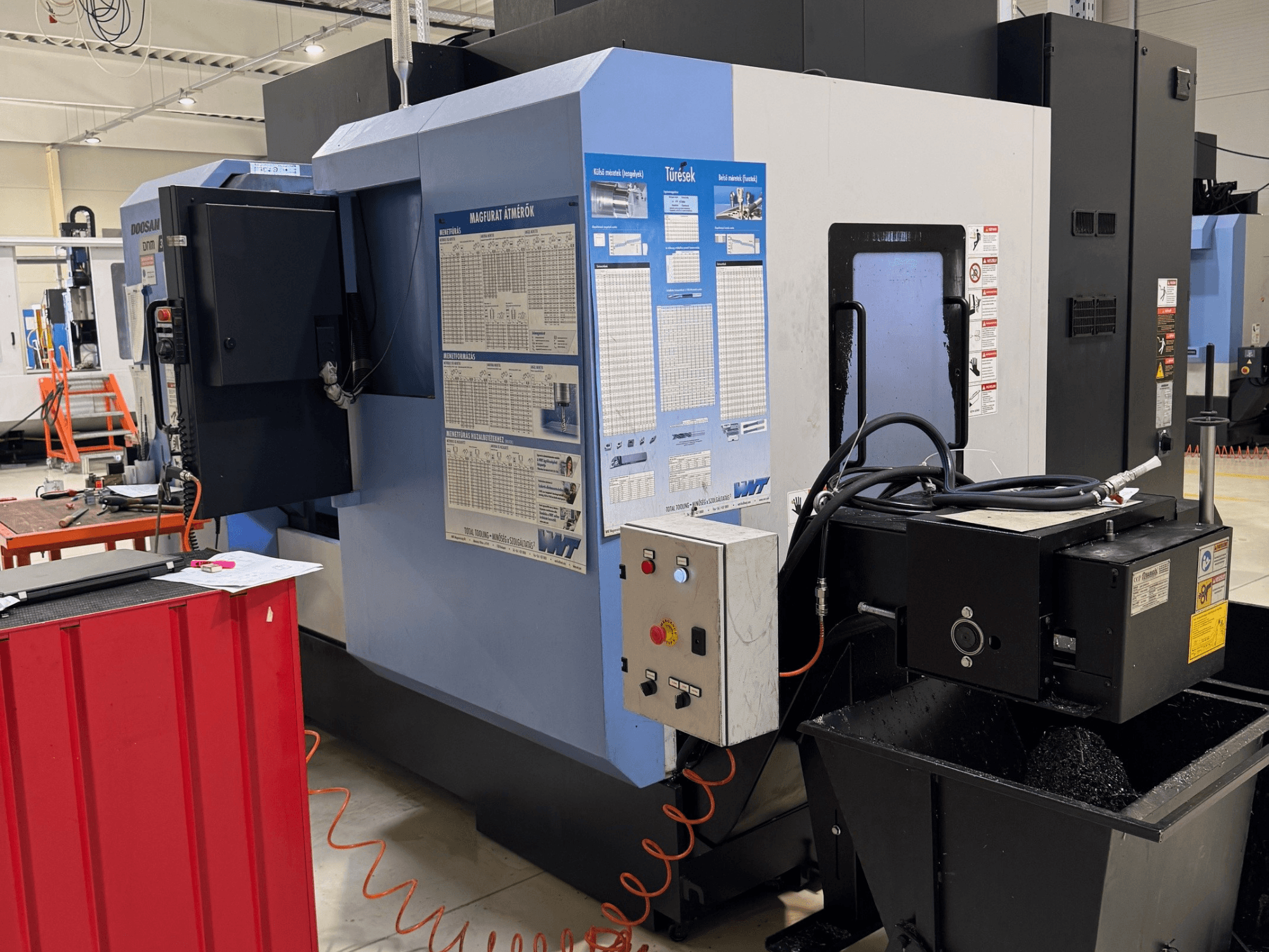 Centro de fresado y torneado DOOSAN DNM350/5AX, vista lateral en la que se aprecian el panel de control y el depósito de refrigerante, con detalles operativos visibles.