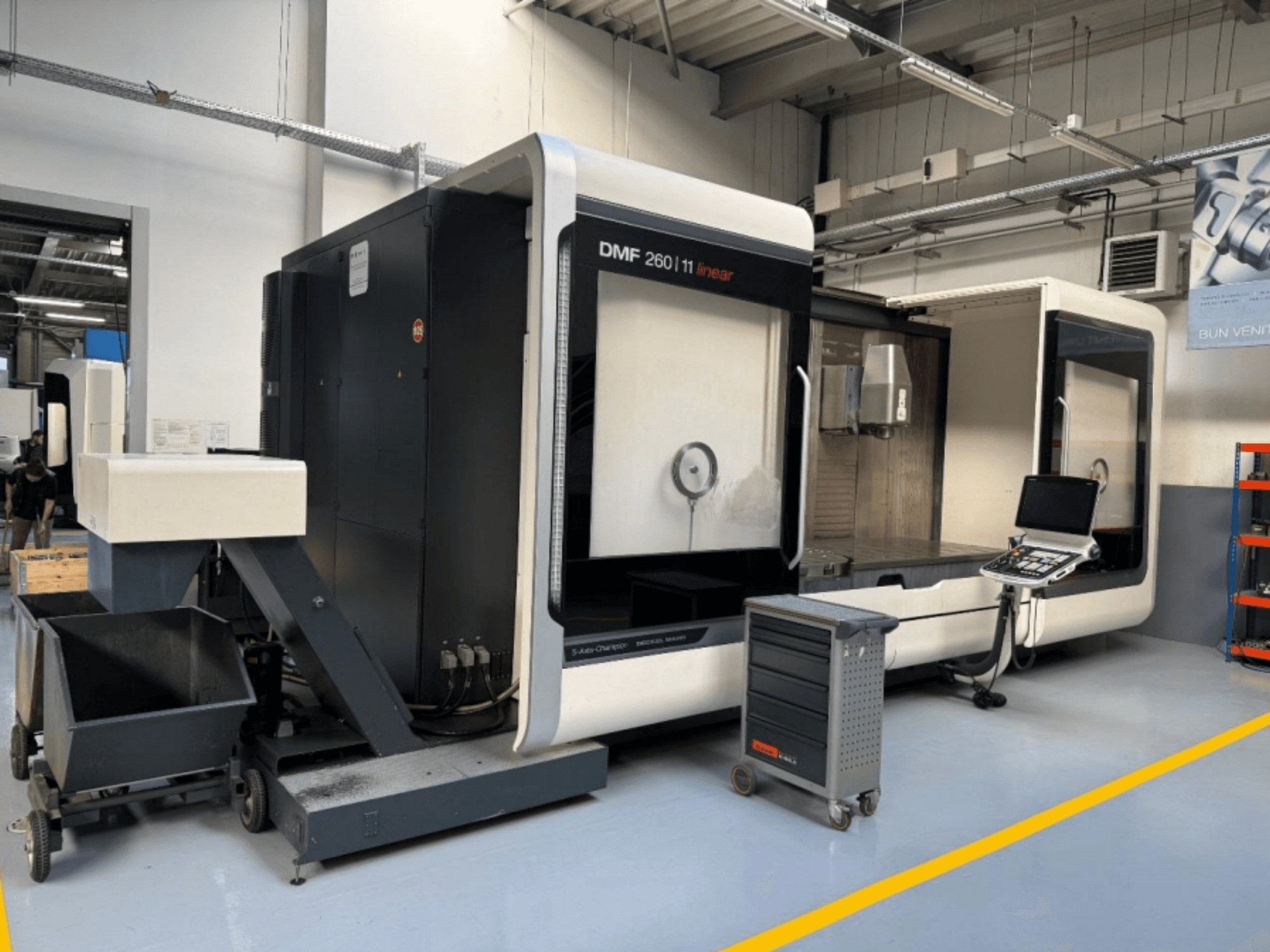 DMG MORI DMF 260 Fresadora lineal mostrada de frente, con un panel de control de herramientas y un carro de herramientas móvil cerca.
