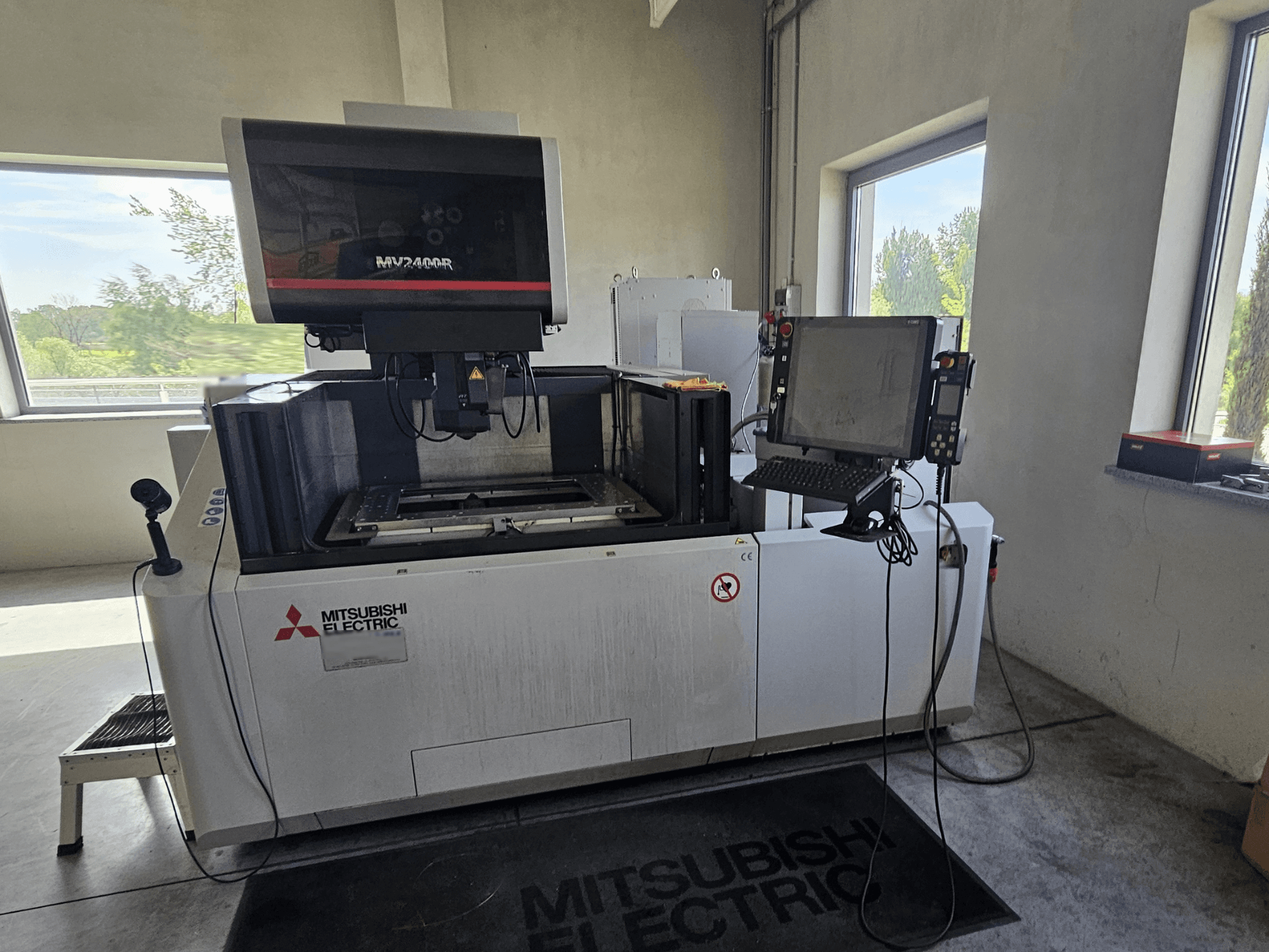 Máquina de electroerosión por hilo Mitsubishi MV2400R en un taller, con panel de control de pantalla táctil y zona de trabajo.