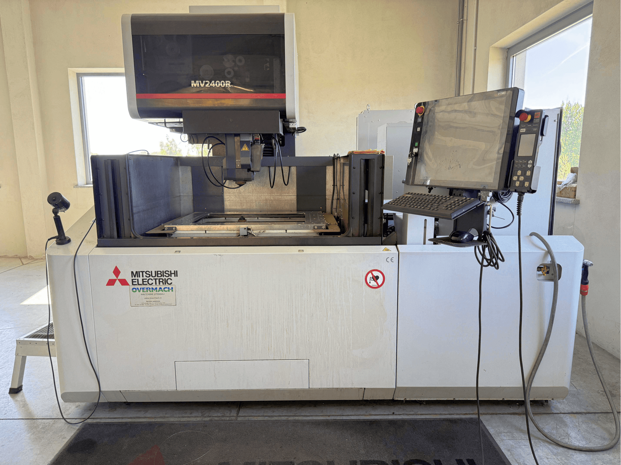 Máquina de electroerosión por hilo Mitsubishi MV2400R vista de frente, en la que se aprecian el panel de control, el espacio de trabajo y la señalización de seguridad.