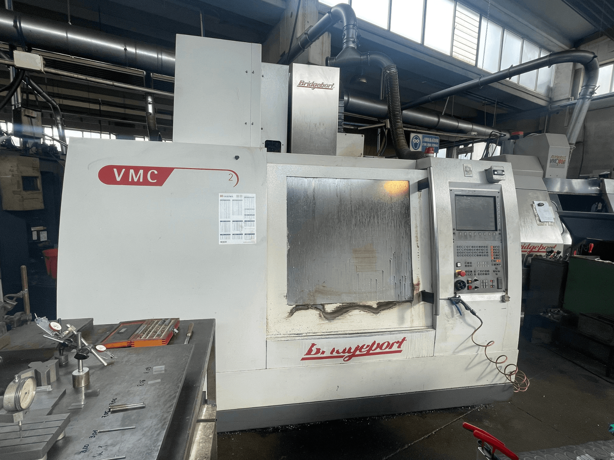 Centro de mecanizado vertical Bridgeport VCM 800-30 en un taller, con panel de control y mesa portaherramientas. Vista frontal con detalles visibles.