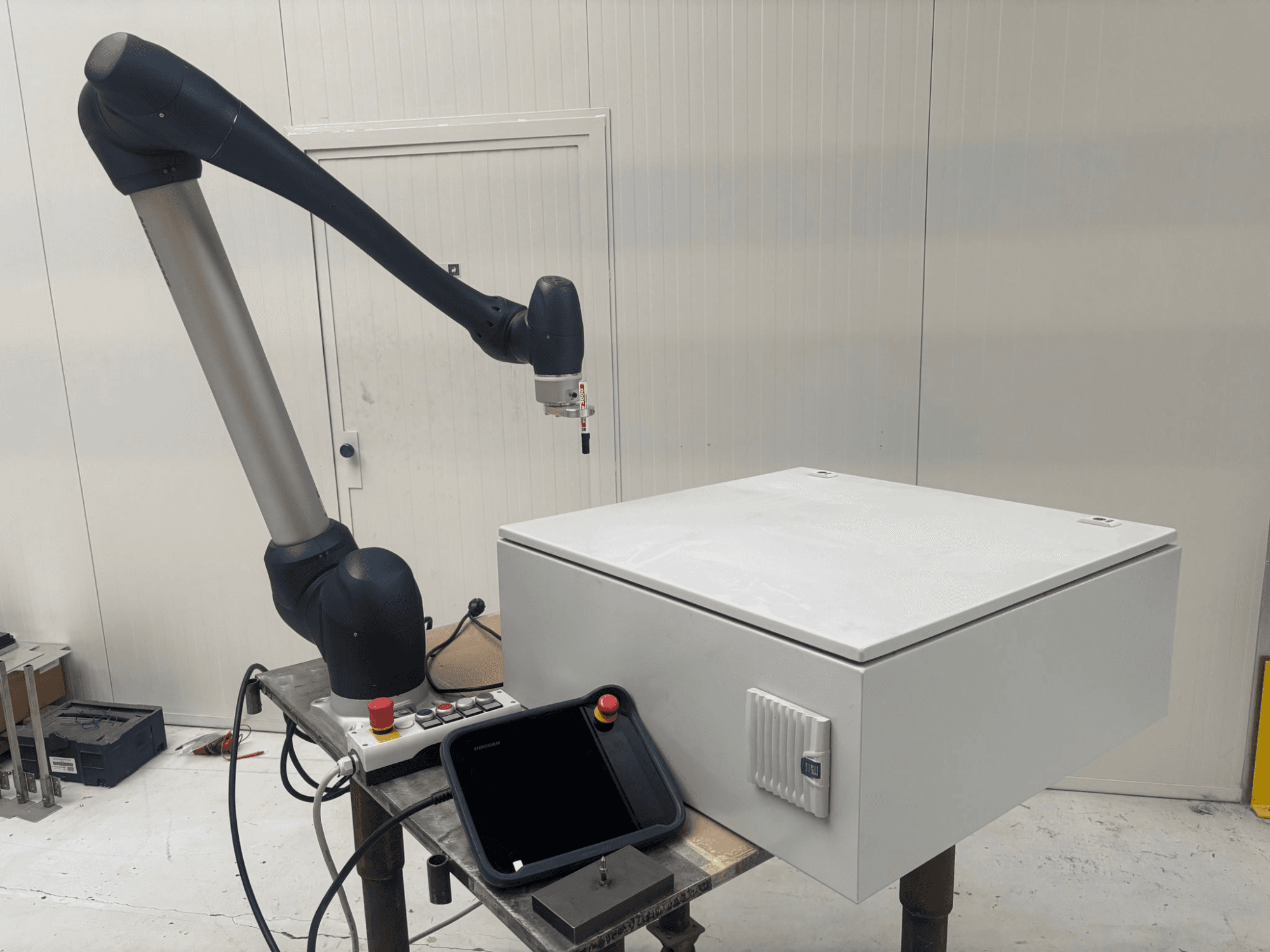Robot colaborativo DOOSAN M0617 en vista lateral, con el brazo robótico extendido sobre una interfaz de control y una caja blanca sobre una mesa.