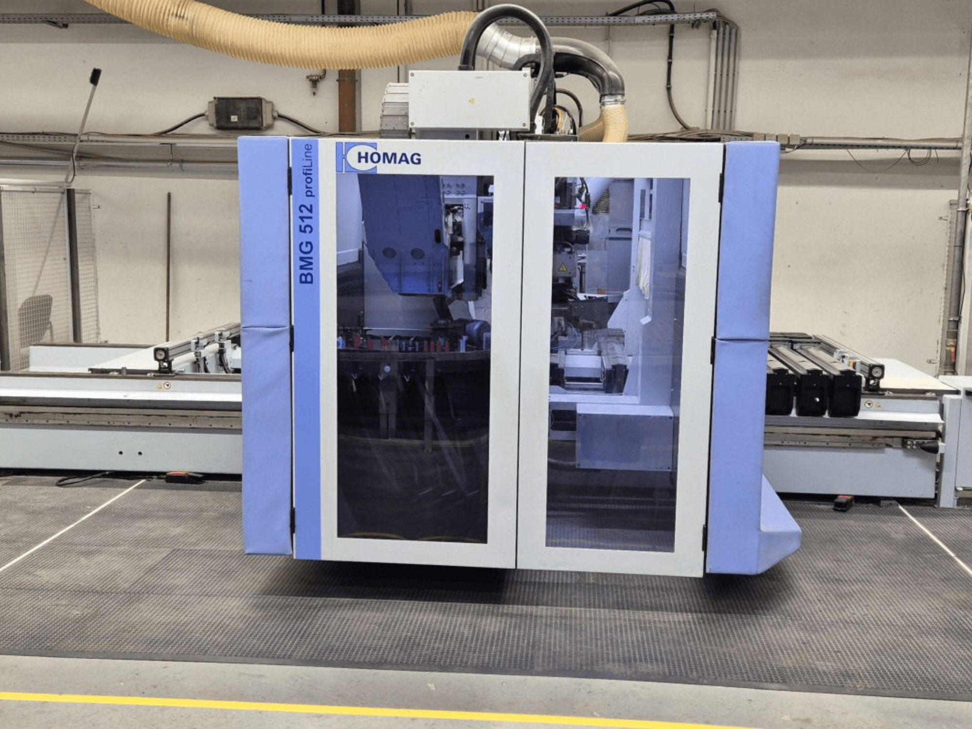 Máquina CNC HOMAG BMG 512 ProfiLine, vista frontal, con panel de cristal, herramientas de precisión visibles y entorno industrial.