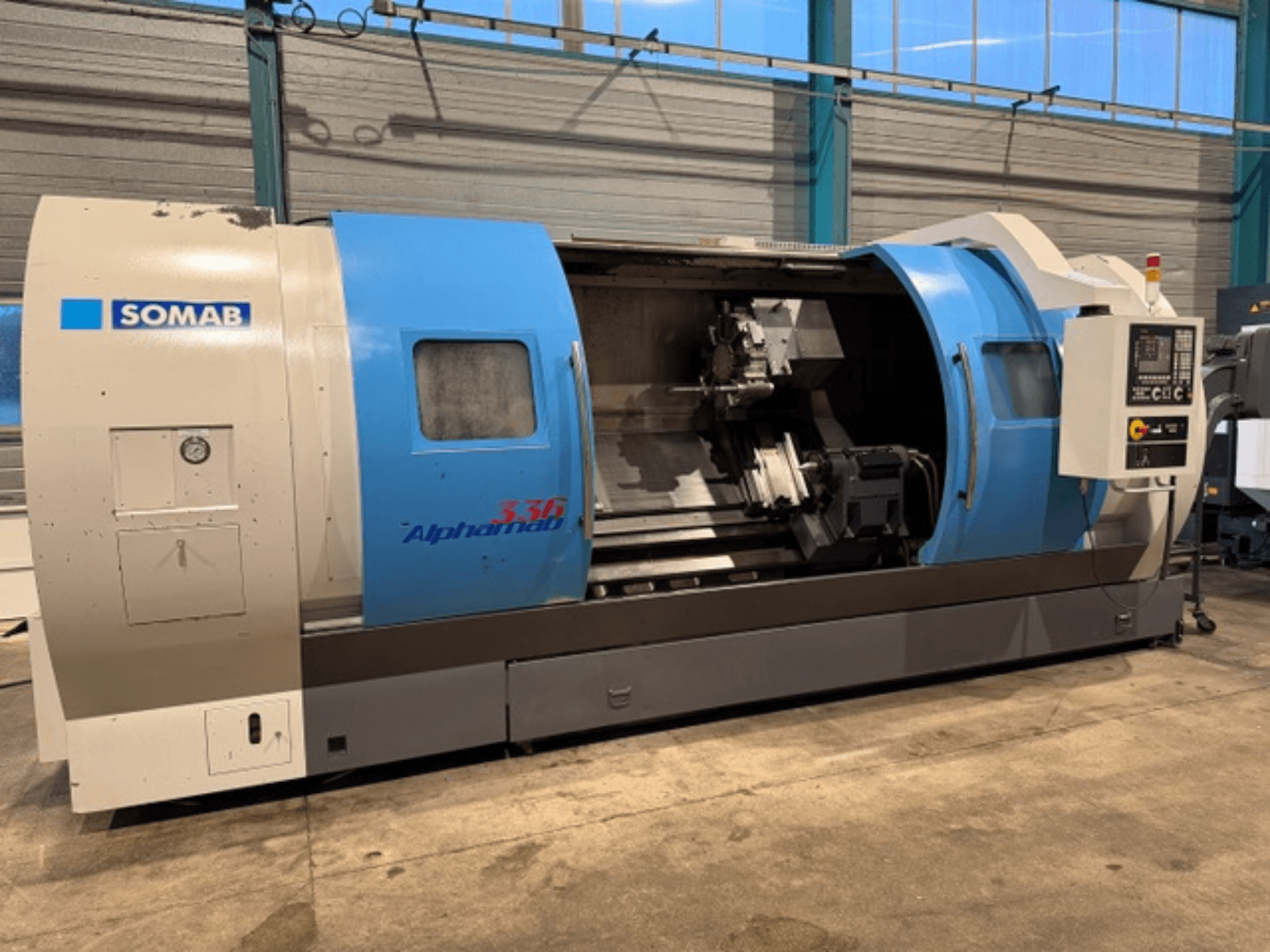 Torno CNC SOMAB Alpha 336, vista frontal, con carcasa azul y gris y panel de control lateral para su manejo.