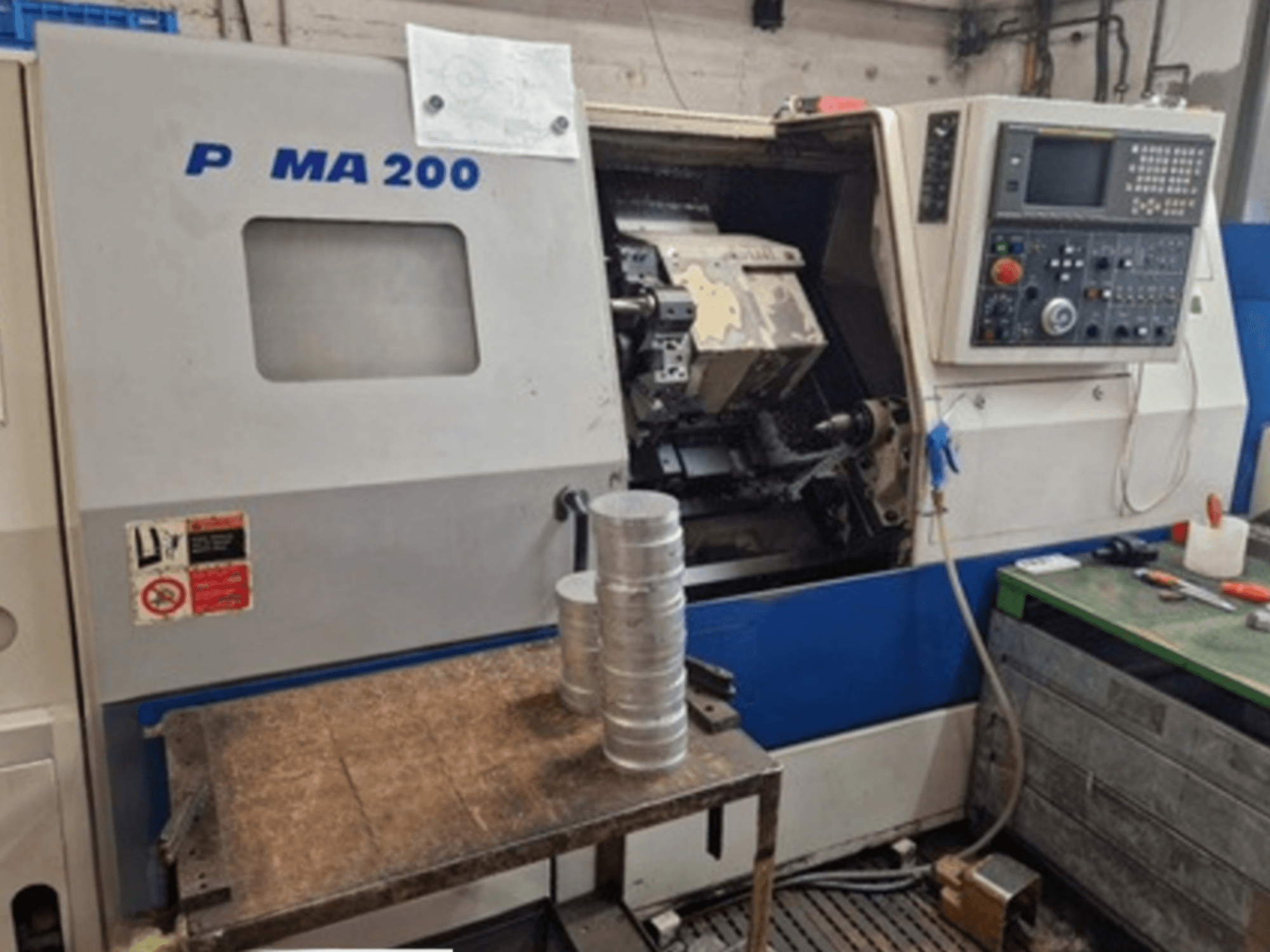 Máquina de torneado horizontal DAEWOO EcoTurn 200, vista frontal, con piezas de aluminio sobre una mesa, panel de control visible.