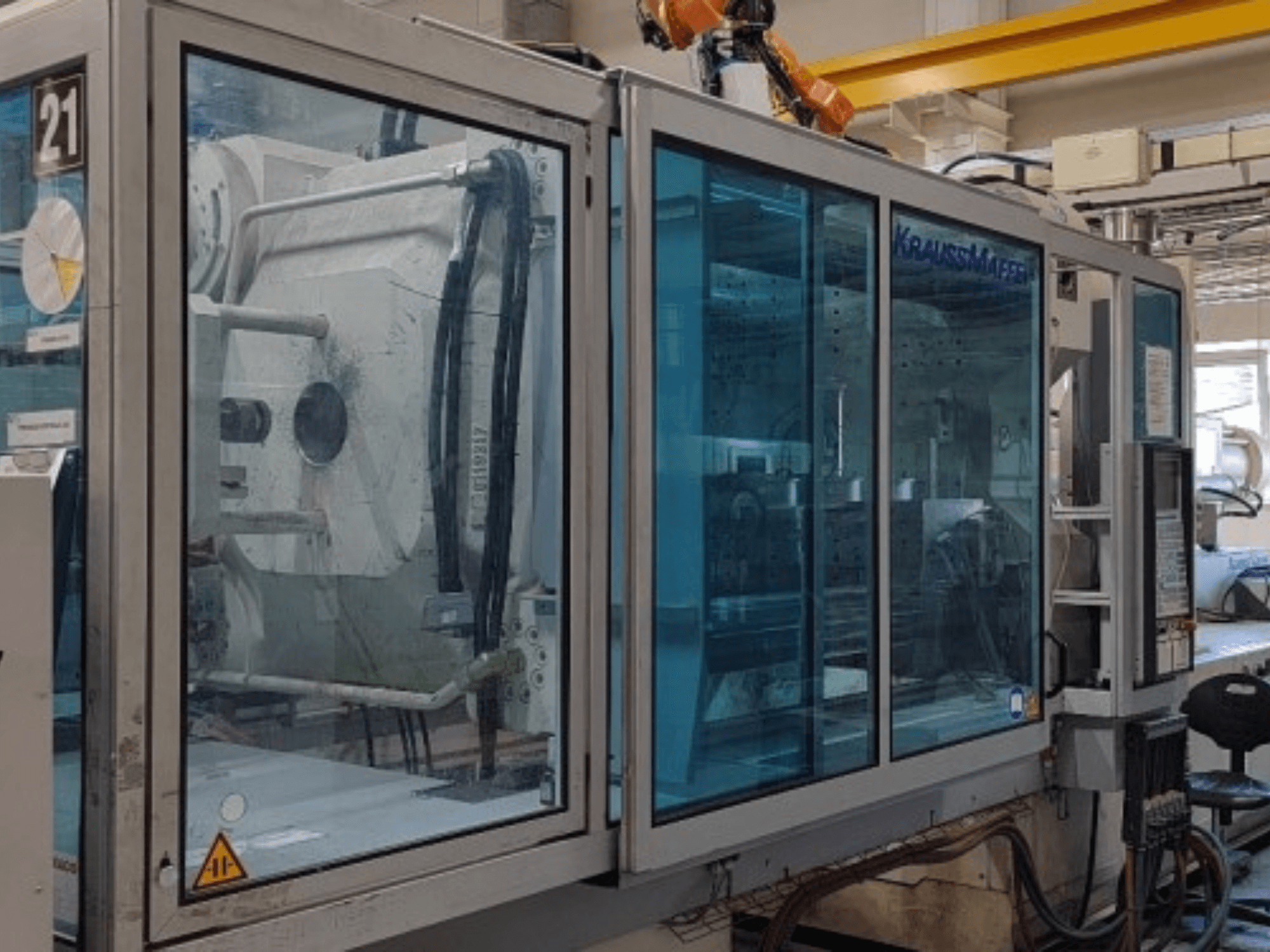 Máquina de moldeo por inyección hidráulica Krauss Maffei KM 575-2700 C2, vista lateral, con paneles de seguridad transparentes y panel de control.