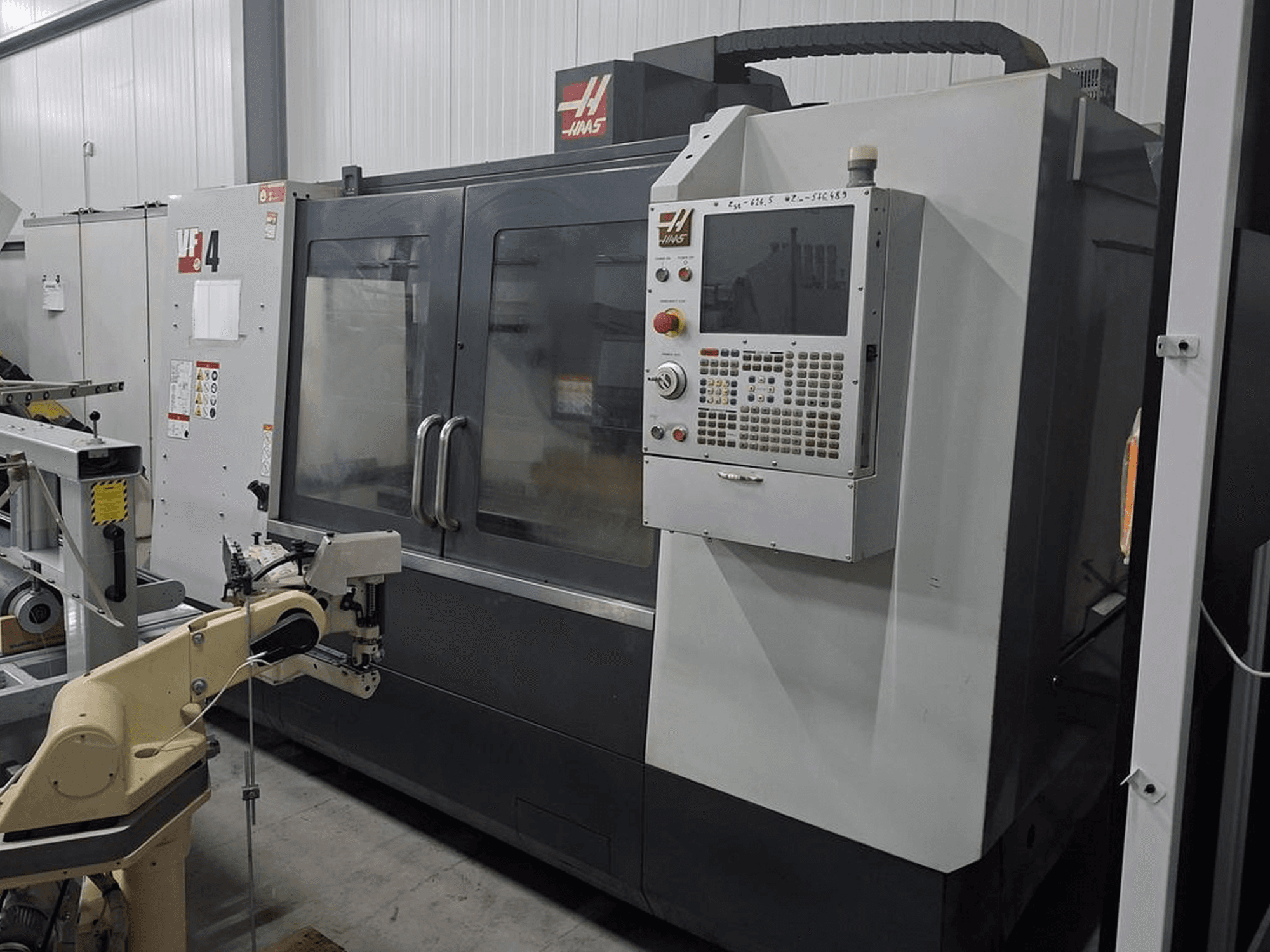 Fresadora CNC Haas VF-4 en vista frontal, con panel de control numérico y brazo robótico para automatización.