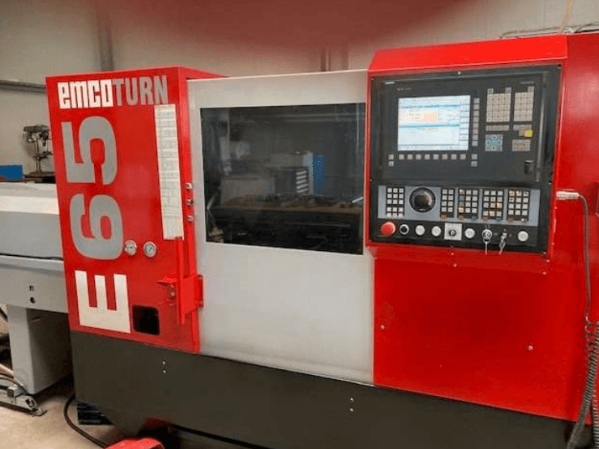 Torno CNC EMCO Turn E65, vista frontal que muestra el panel de control, la gran pantalla y el área de trabajo detrás del cristal.