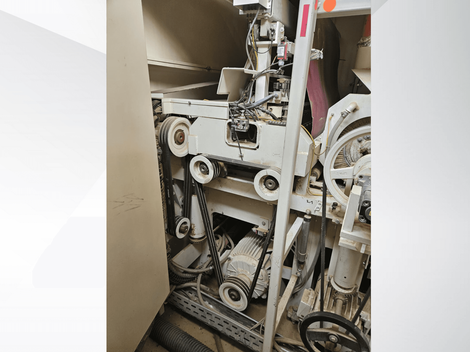 Interior de máquina industrial con correas y poleas, con motor y cableado, vista de lado.