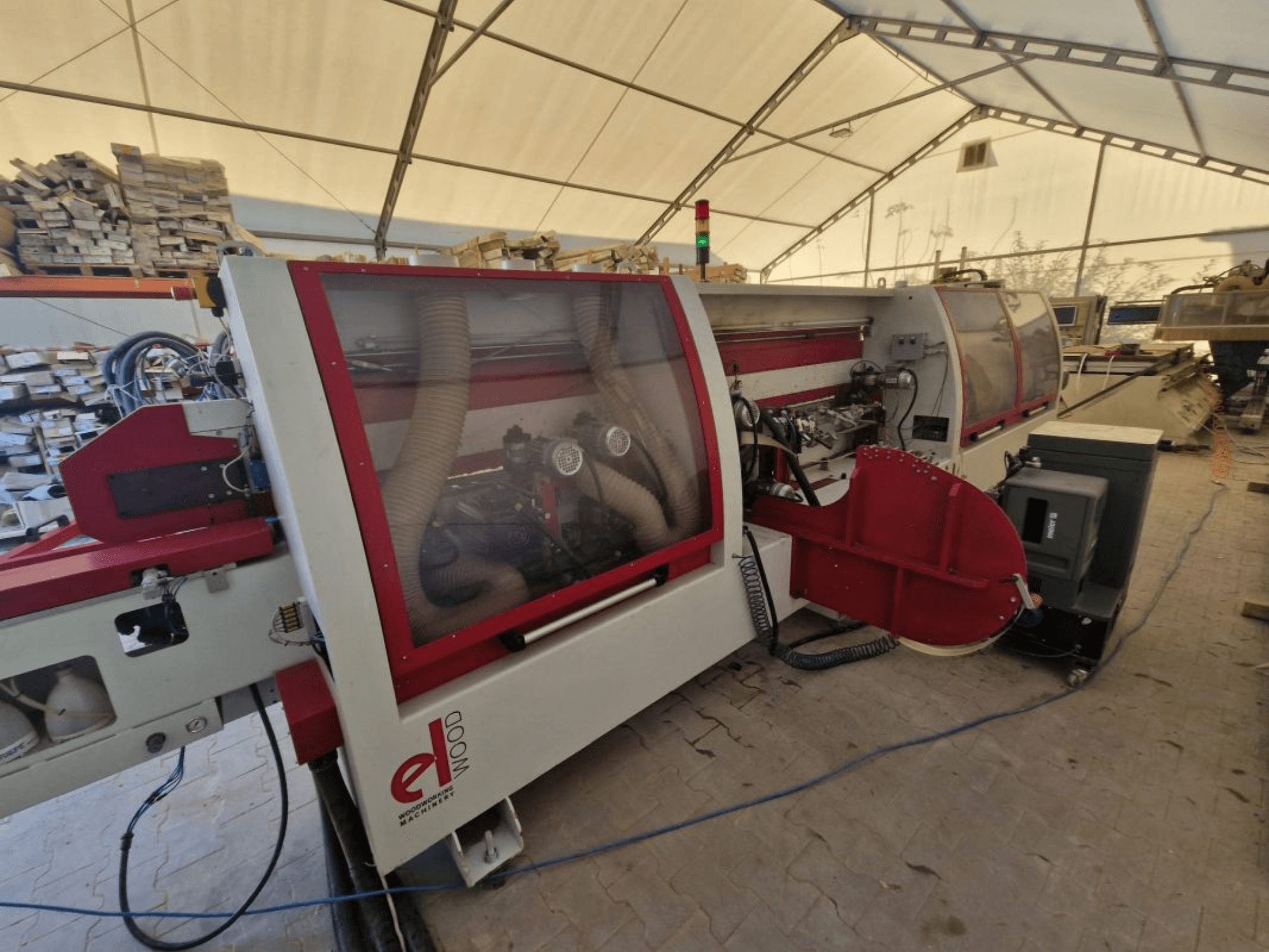 Máquina encintadora ELWOOD EDL SOFT, vista lateral que muestra el sistema de aspiración de polvo y los mandos en el interior de un taller con pilas de madera.