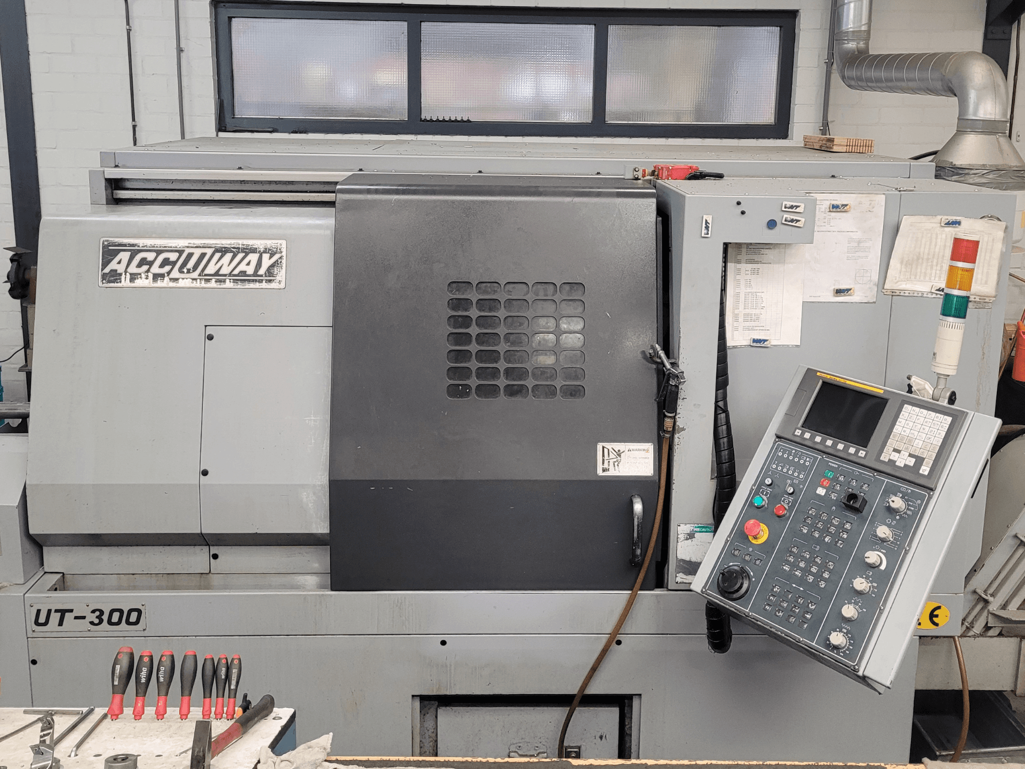 Vista frontal de la máquina CNC Accuway UT-300, con un panel de control y varios botones de funcionamiento, en un taller.
