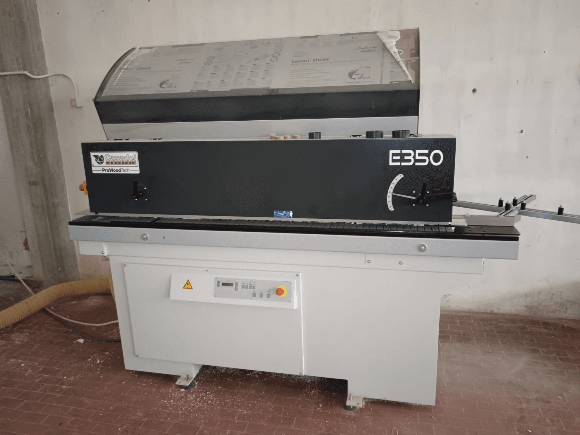 Cesaroli ProWoodtech E350, vista lateral de una máquina para trabajar la madera con panel de control y acumulación de polvo, montada sobre una base blanca.