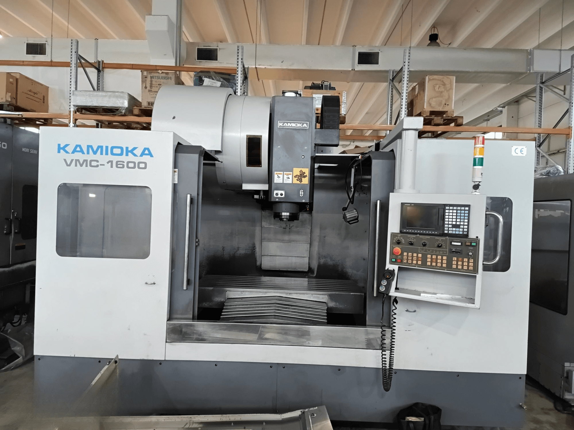 Centro de mecanizado vertical Kamioka VMC-1600 en un entorno de fábrica, vista frontal con panel de control y bancada de mecanizado visible.