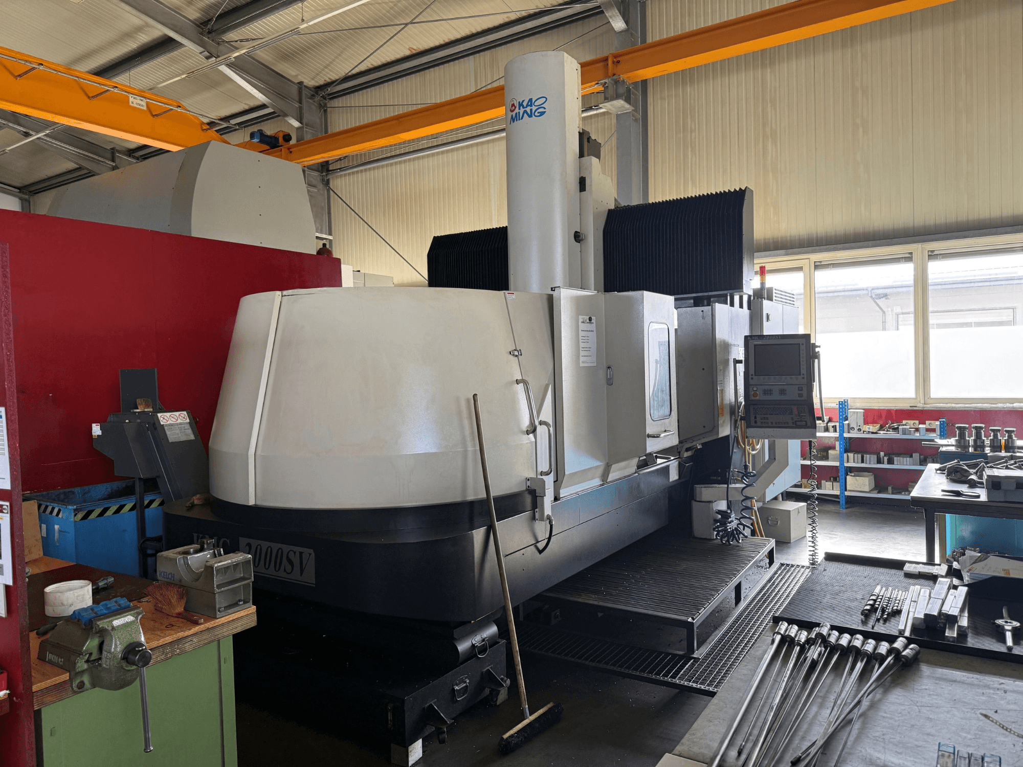 Fresadora de pórtico KAOMING KMC-2000 SV en un taller, vista frontal en la que se aprecian el panel de control y las herramientas circundantes.