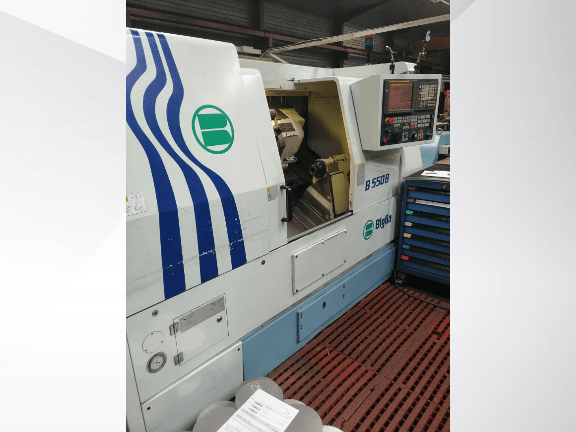 Máquina de torno CNC Biglia B 550 B mostrada de frente, con panel de control, área de trabajo en metal y colorido almacenamiento de herramientas.