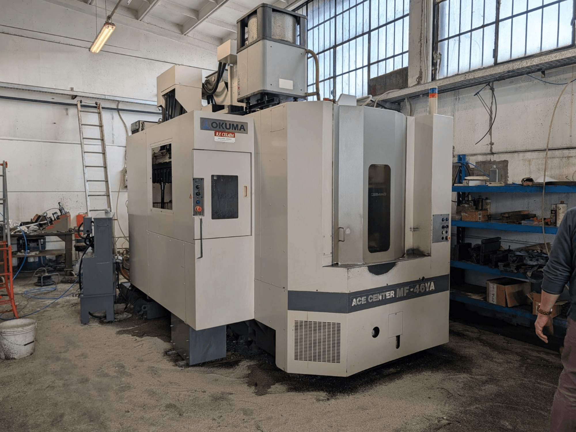 Centro de mecanizado vertical Okuma ACE CENTER MF-46VA en un taller, mostrando la vista frontal con el panel de control y el equipo circundante.