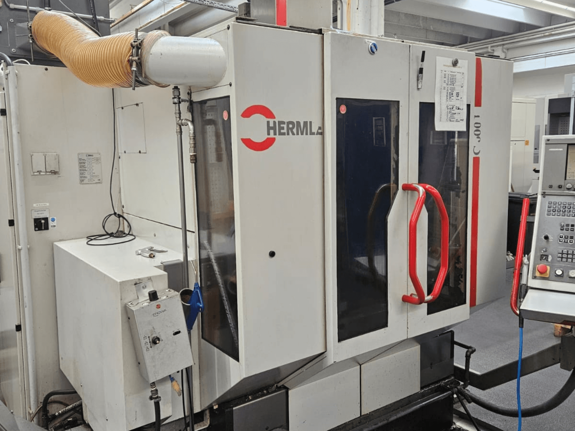 Vista frontal del centro de mecanizado universal HERMLE C 600 U, mostrando el panel de control y los tiradores rojos de las puertas.