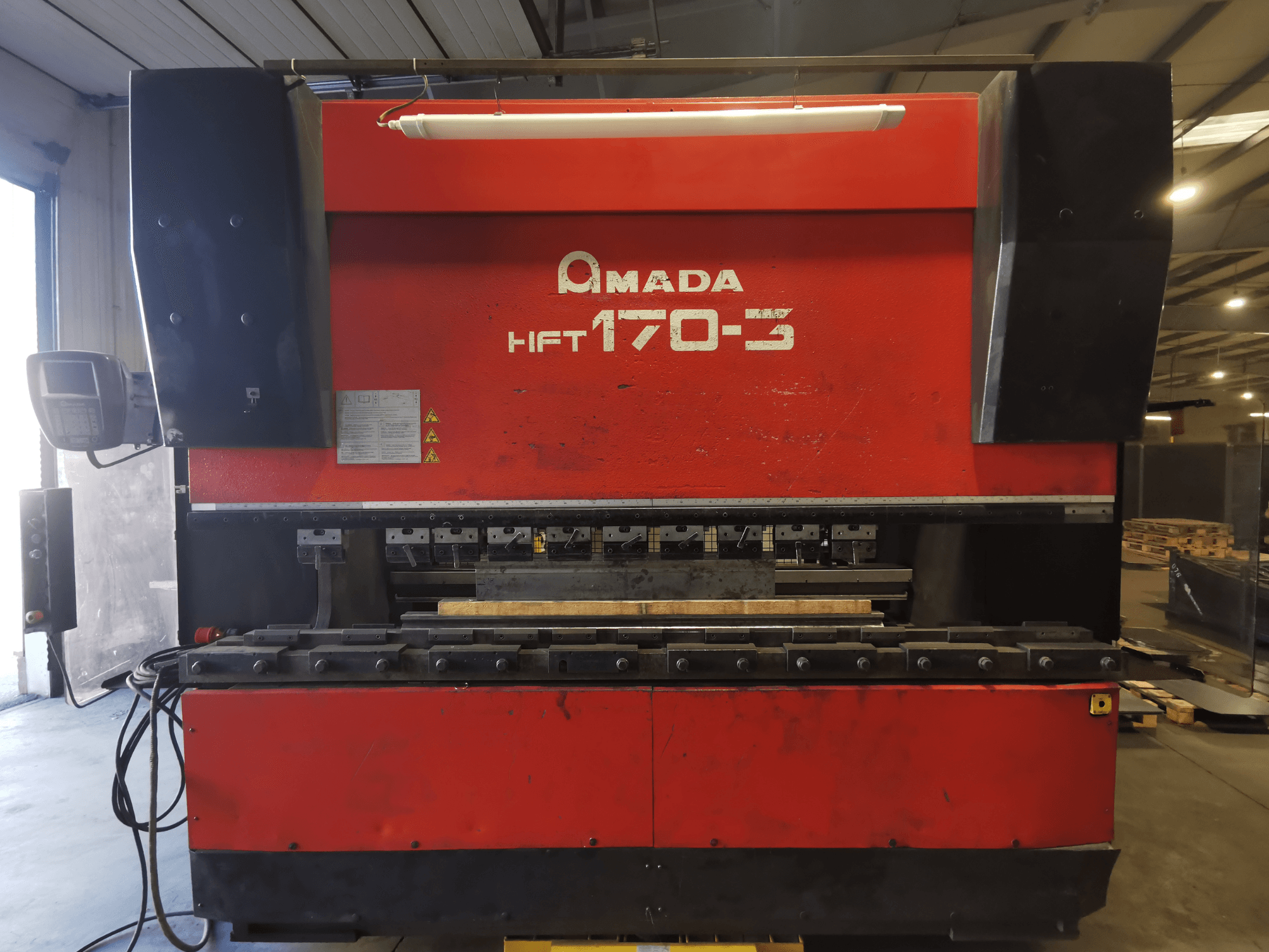 Plegadora Amada HFT 170-3 roja vista de frente, mostrando el panel de control, las herramientas de plegado y la superficie de trabajo.