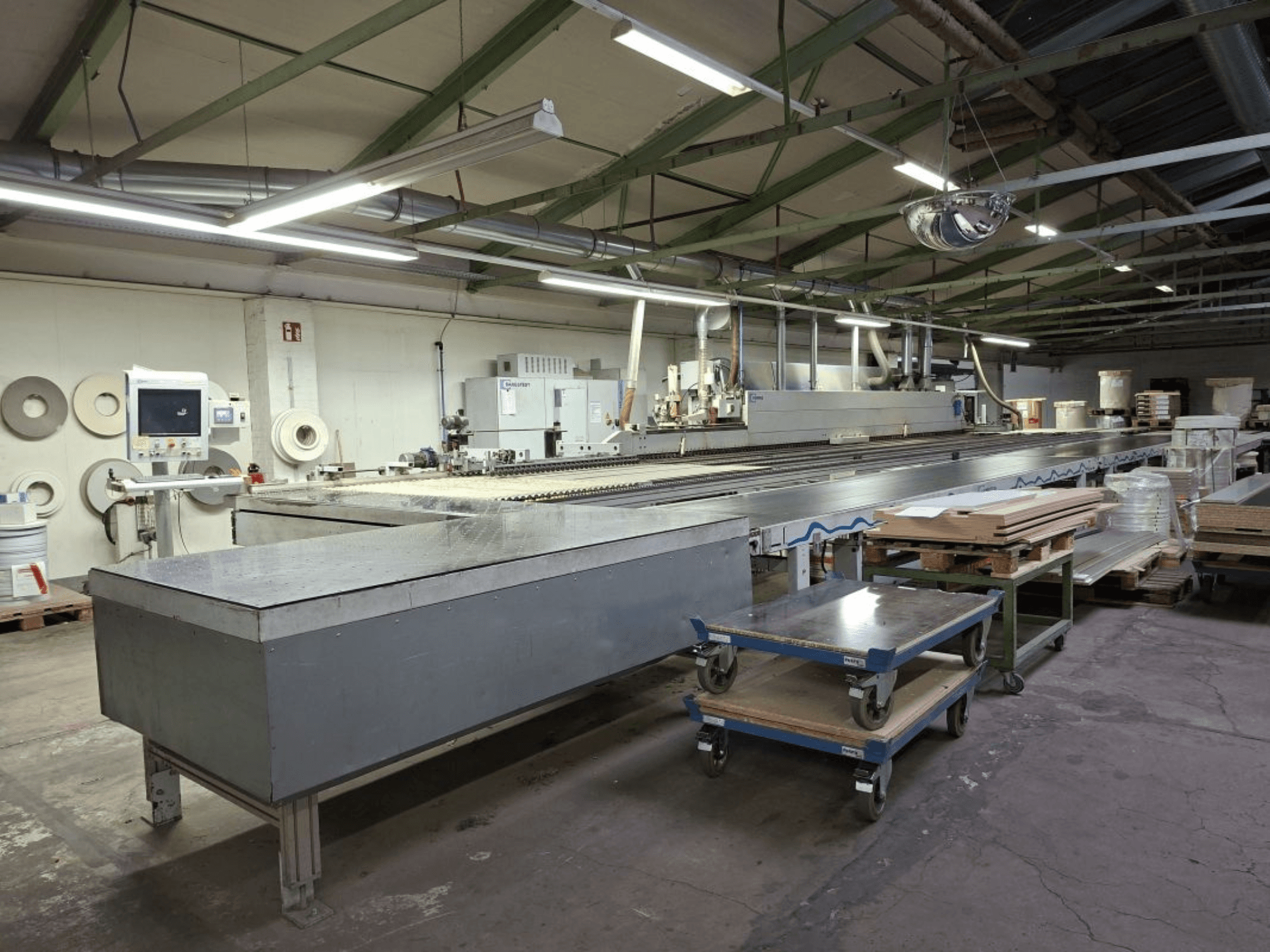La chapadora de cantos Optimat KAL 330 de HOMAG vista desde un lateral, con una larga mesa transportadora y panel de control en un taller.