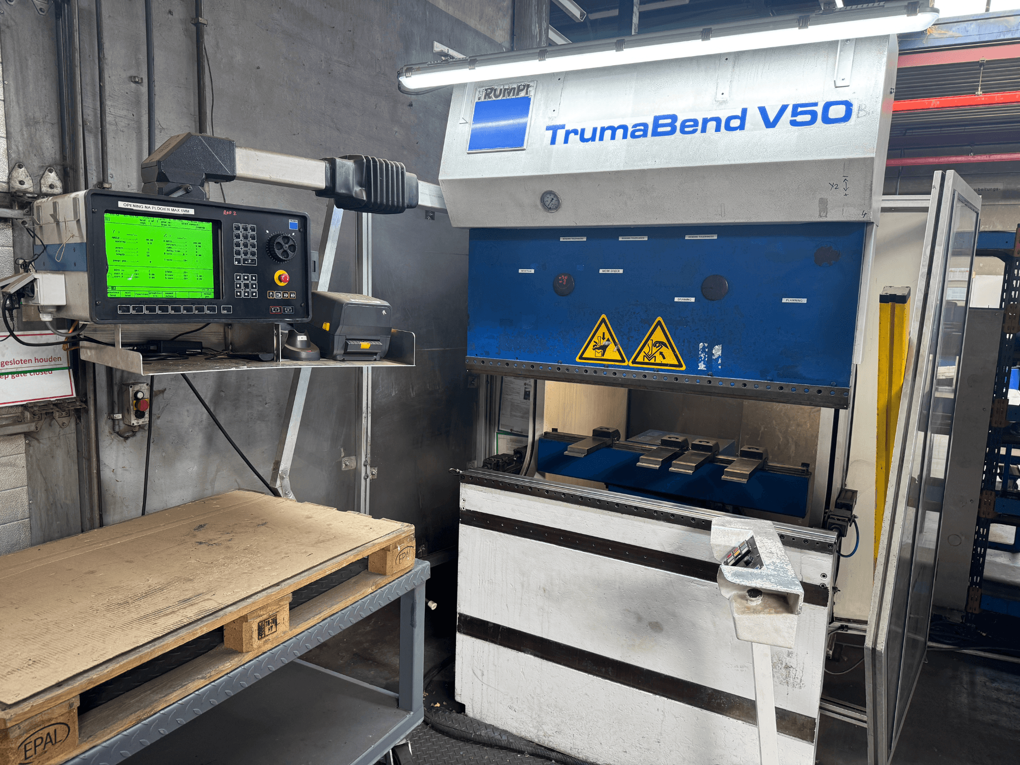Plegadora TRUMPF TrumaBend V50, vista frontal, con panel de control que muestra los ajustes y las señales de advertencia de seguridad.