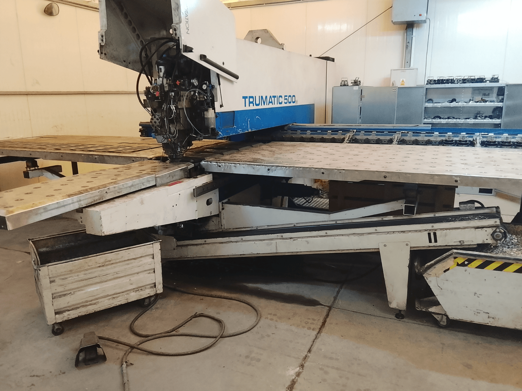 Máquina CNC TRUMATIC 500 en un taller, vista lateral que muestra el cabezal de corte y la mesa de trabajo metálica con orificios pretaladrados.