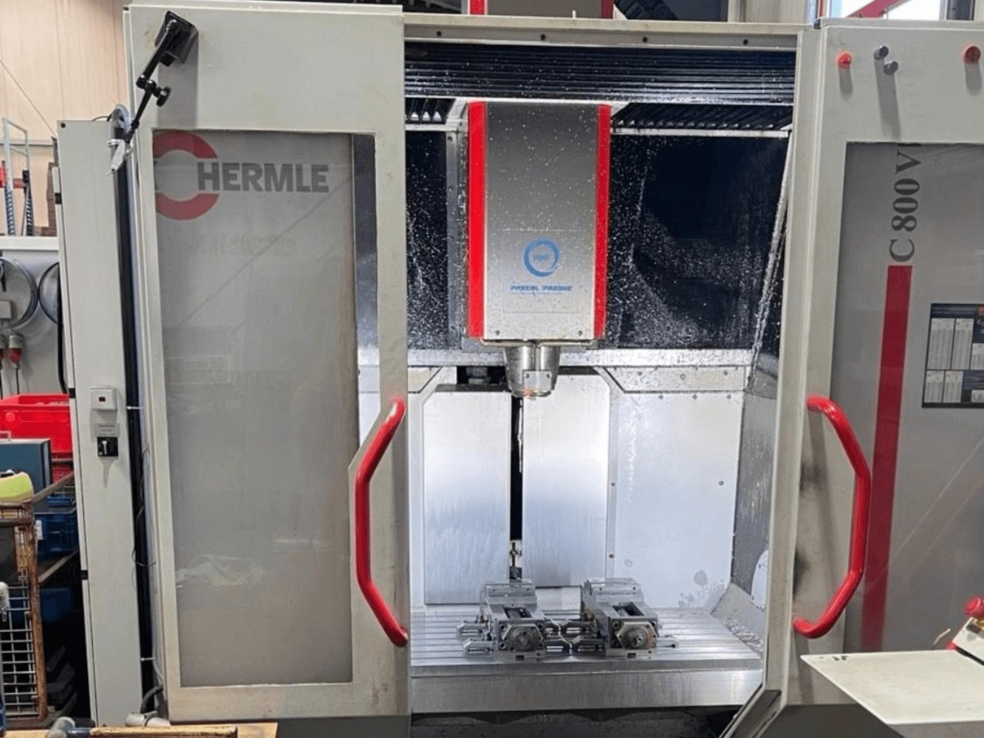 Centro de mecanizado vertical HERMLE C800V; vista frontal en la que se aprecia la zona de mecanizado con las piezas y el líquido refrigerante.