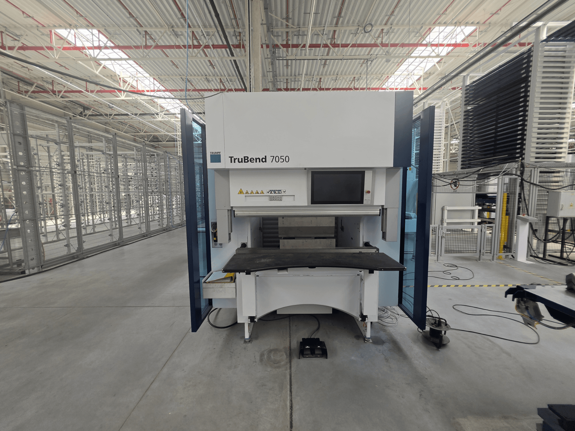 Vista frontal de la plegadora TRUMPF TruBend 7050, en la que se aprecian el panel de control y la mesa de trabajo en un entorno industrial bien iluminado.
