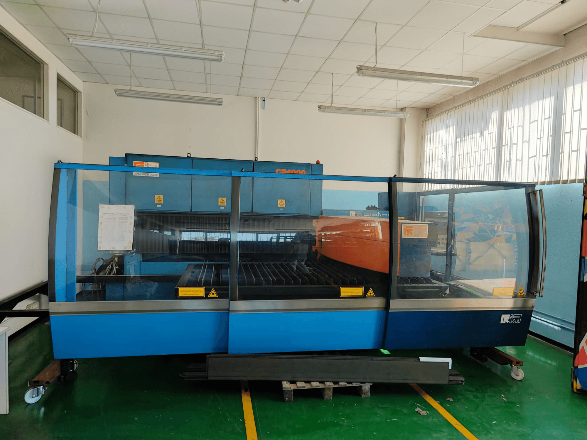 Vista frontal de una máquina de corte por láser de CO₂ CP4000 de CONVERGENT LASERS, con un diseño en azul y naranja, en un taller bien iluminado.