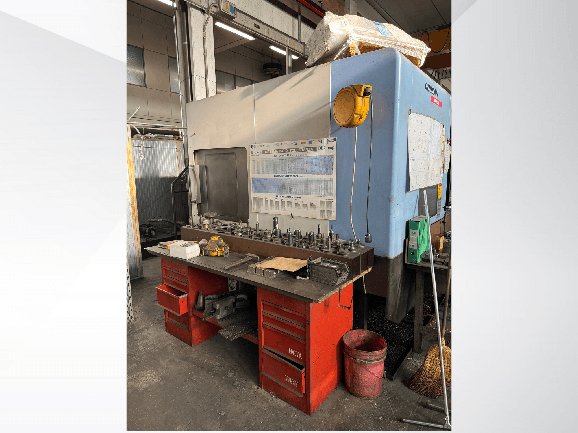 Centro de mecanizado Doosan con un banco de trabajo rojo y almacenamiento, que muestra herramientas y equipos, visto de frente.