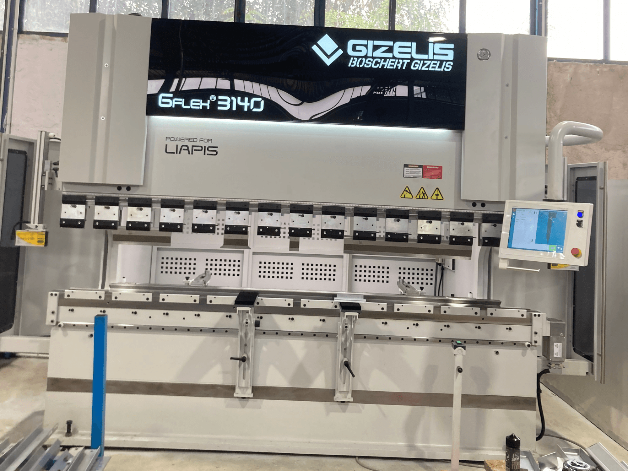 Prensa hidráulica GIZELIS G-FLEX 3140 en vista frontal con pantalla de control, con múltiples herramientas de plegado y etiquetas de seguridad.
