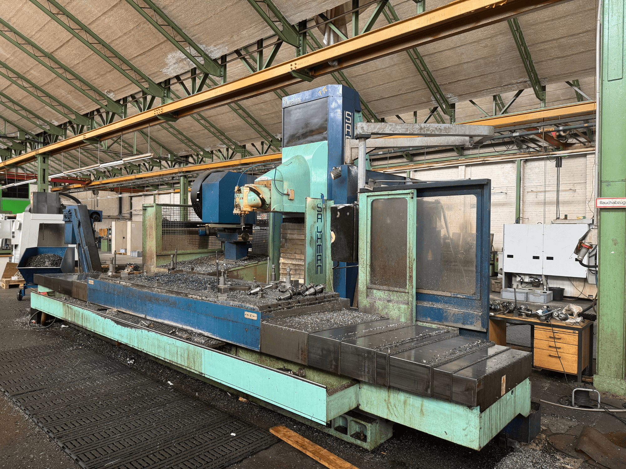 Fresadora Salvador en configuración de fábrica, vista frontal, con un esquema de colores azul y verde, mostrando virutas de metal en la cama.