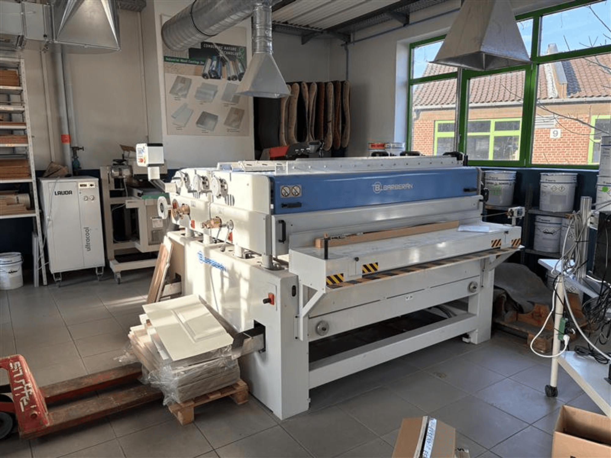 Máquina para trabajar la madera Blaserbn en un taller, vista frontal; con paneles de madera sobre un palé y equipos modernos al fondo.