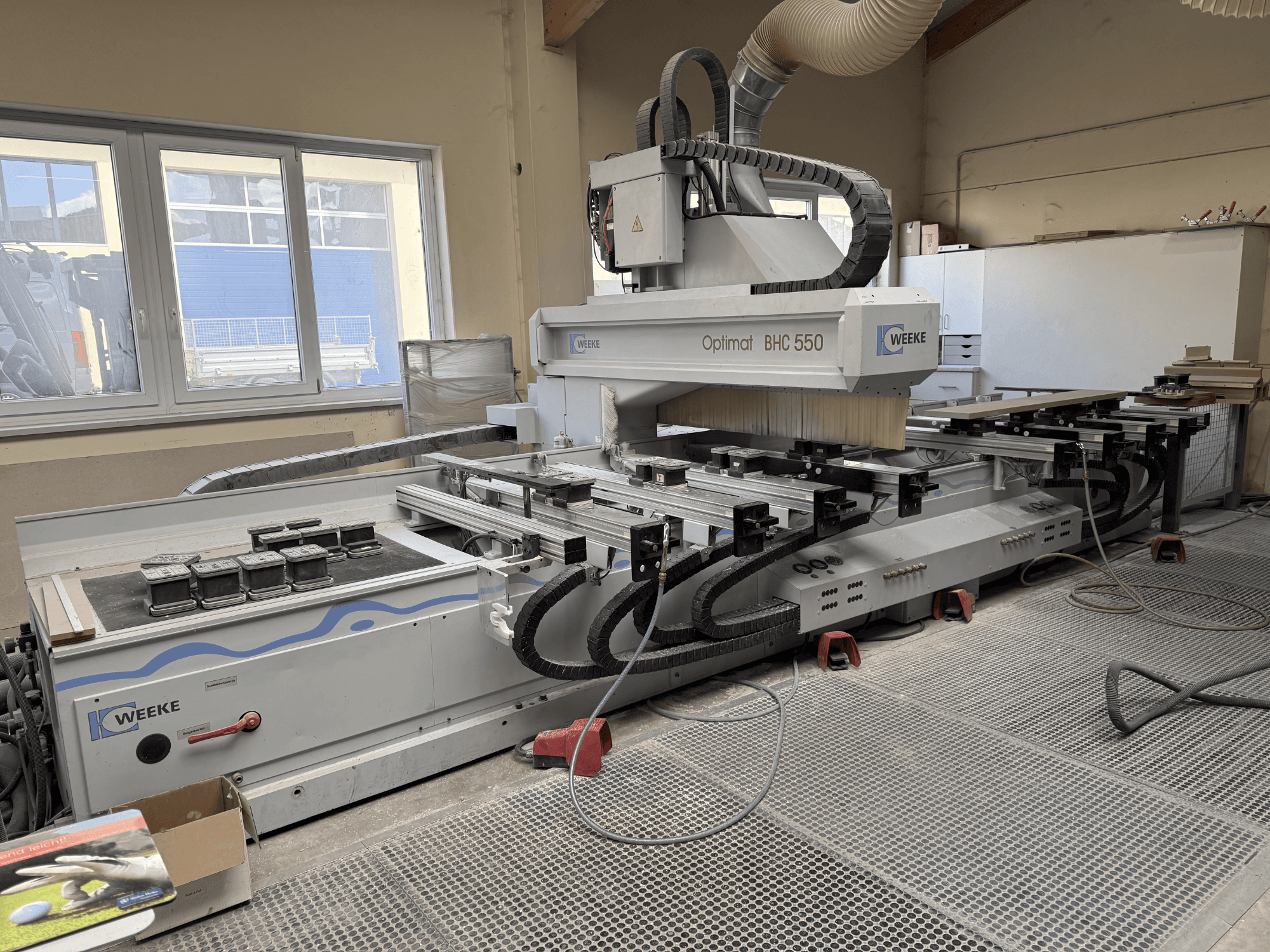 Centro de mecanizado de madera CNC Weeke Optimat BHC 550, vista frontal mostrando el cabezal de herramientas y la mesa de trabajo, con el sistema de extracción de polvo visible.
