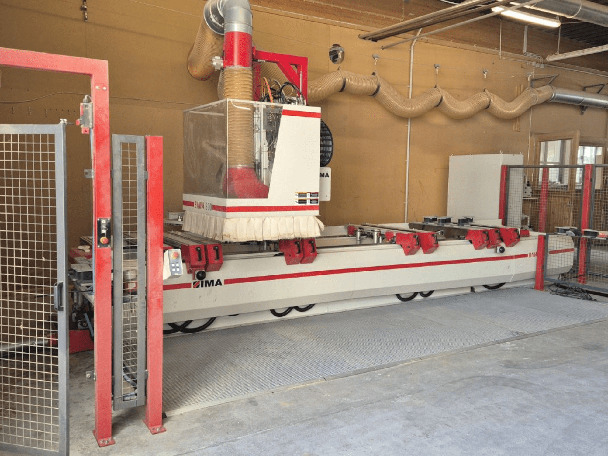 Centro de mecanizado CNC IMA BIMA/300/125/530 en un taller, vista frontal con acentos rojos y cerramiento de seguridad.