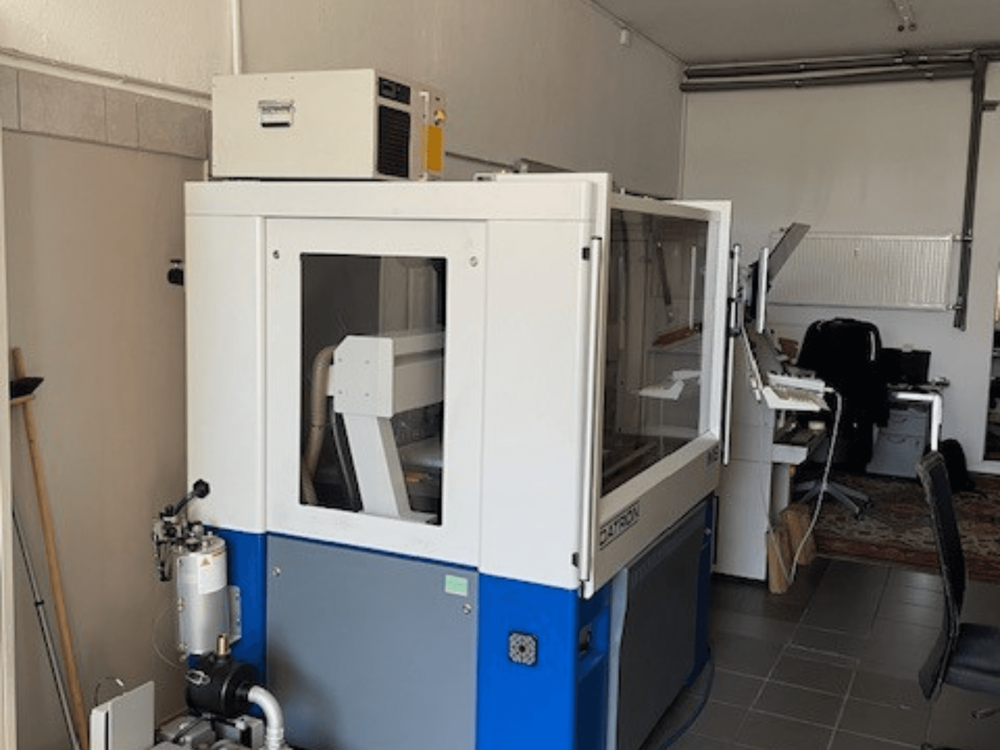 Máquina industrial azul y blanca con paneles transparentes, vista frontal, incluye acceso de control y unidad de ventilación visible.