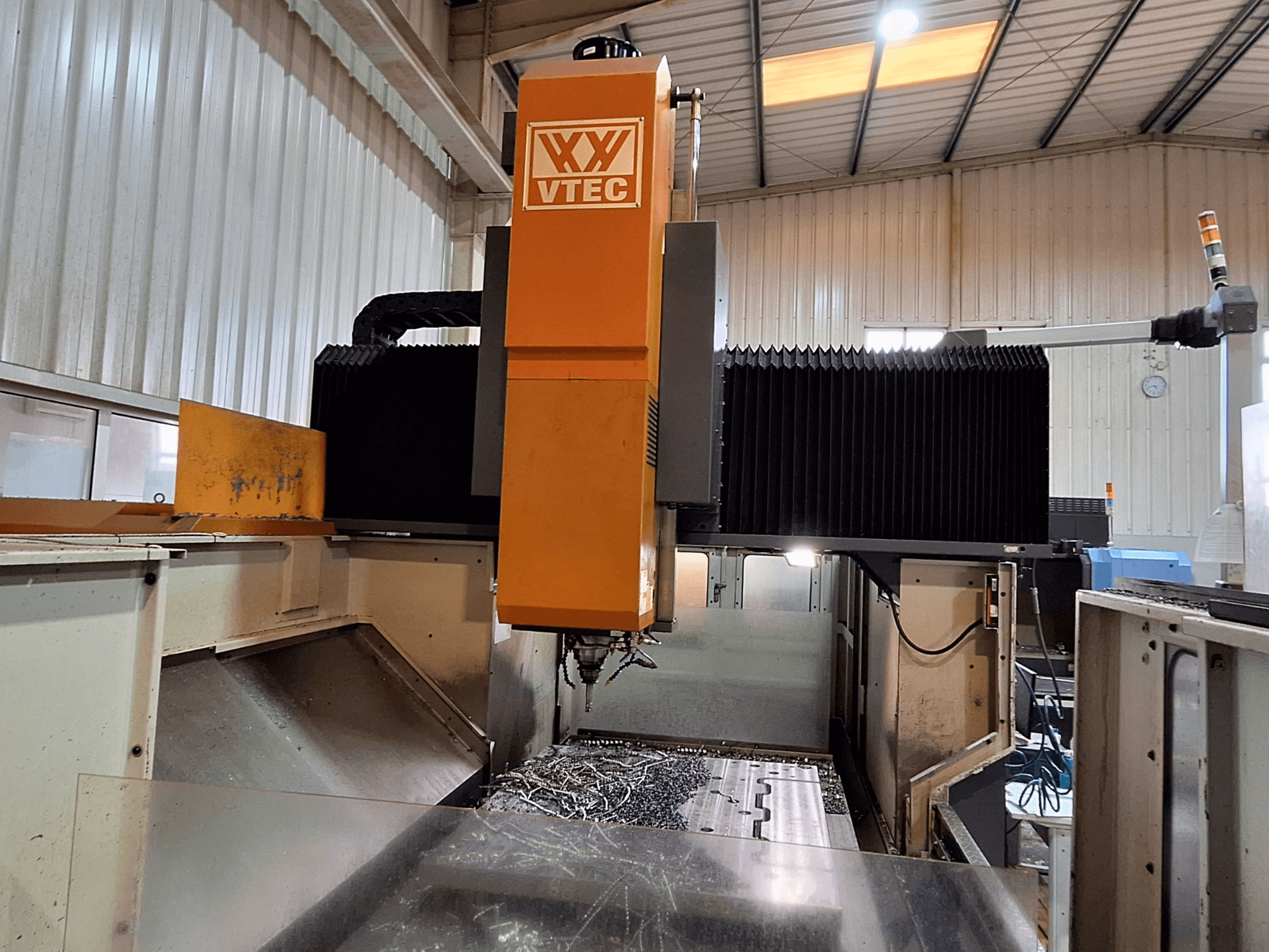 Fresadora de pórtico de PORTIC, modelo VTEC, mostrada desde la vista frontal con la herramienta de corte y las virutas de metal visibles.