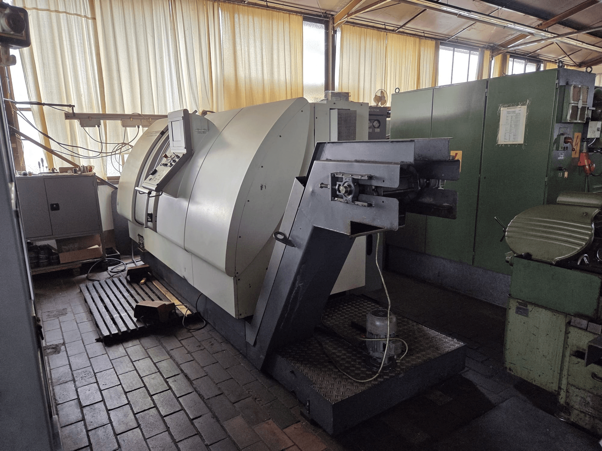 El centro de torneado y fresado doble Gildemeister CTX 400, visto de perfil, muestra el panel de control, el amplio chasis y la maquinaria adyacente en el taller.