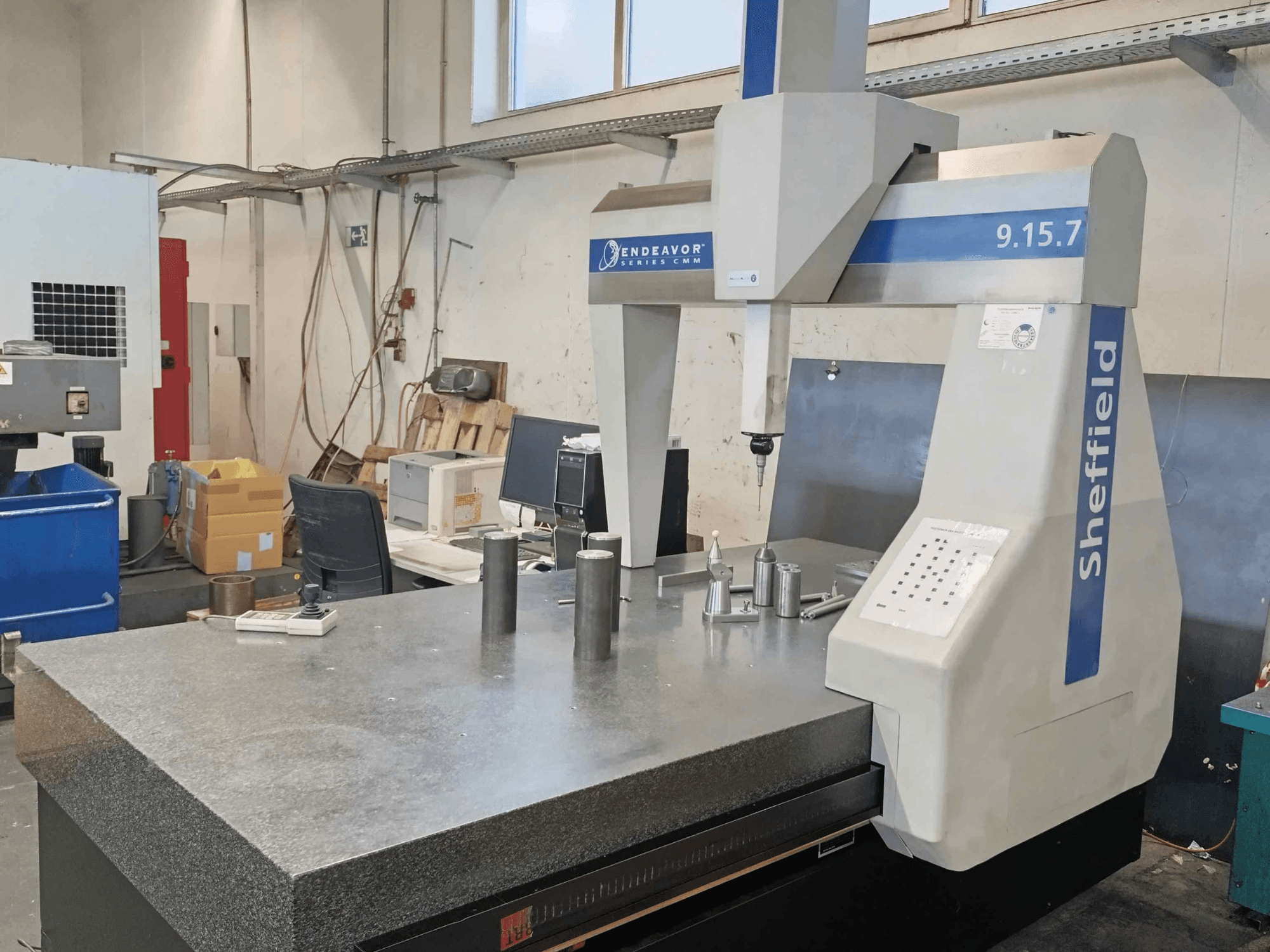 Máquina de medición por coordenadas Sheffield Endeavor 9.15.7 en un taller, con una mesa de granito y piezas metálicas.