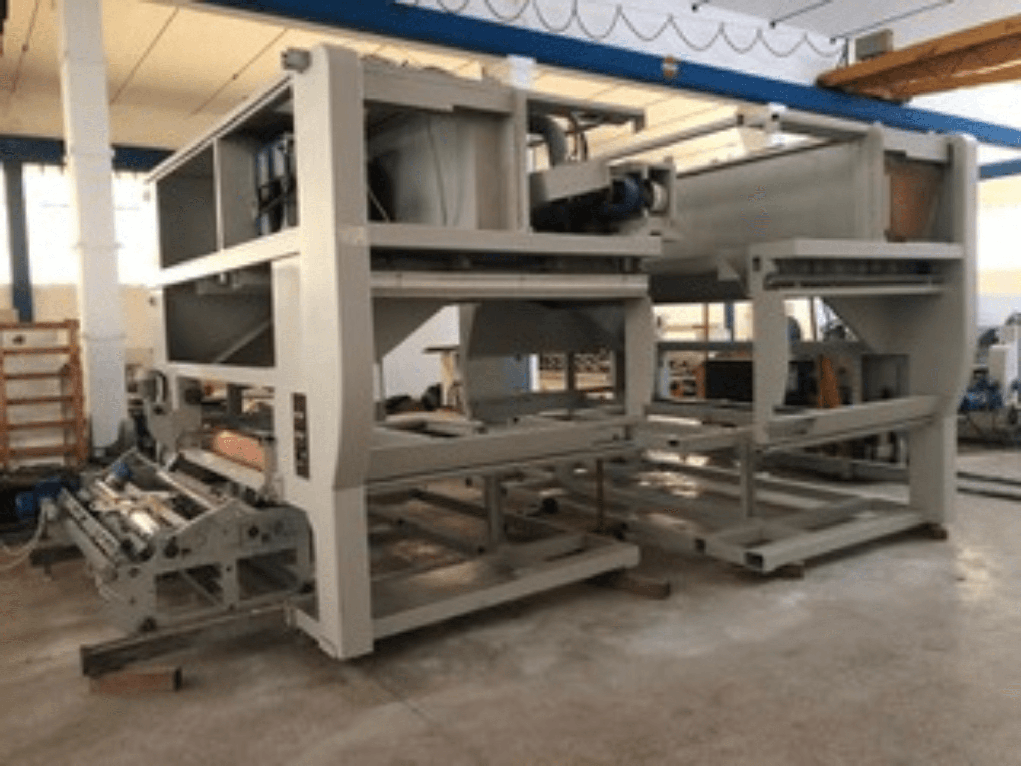 Máquina industrial con múltiples rodillos transportadores y gran estructura; vista lateral, color gris, situada en una fábrica bien iluminada.