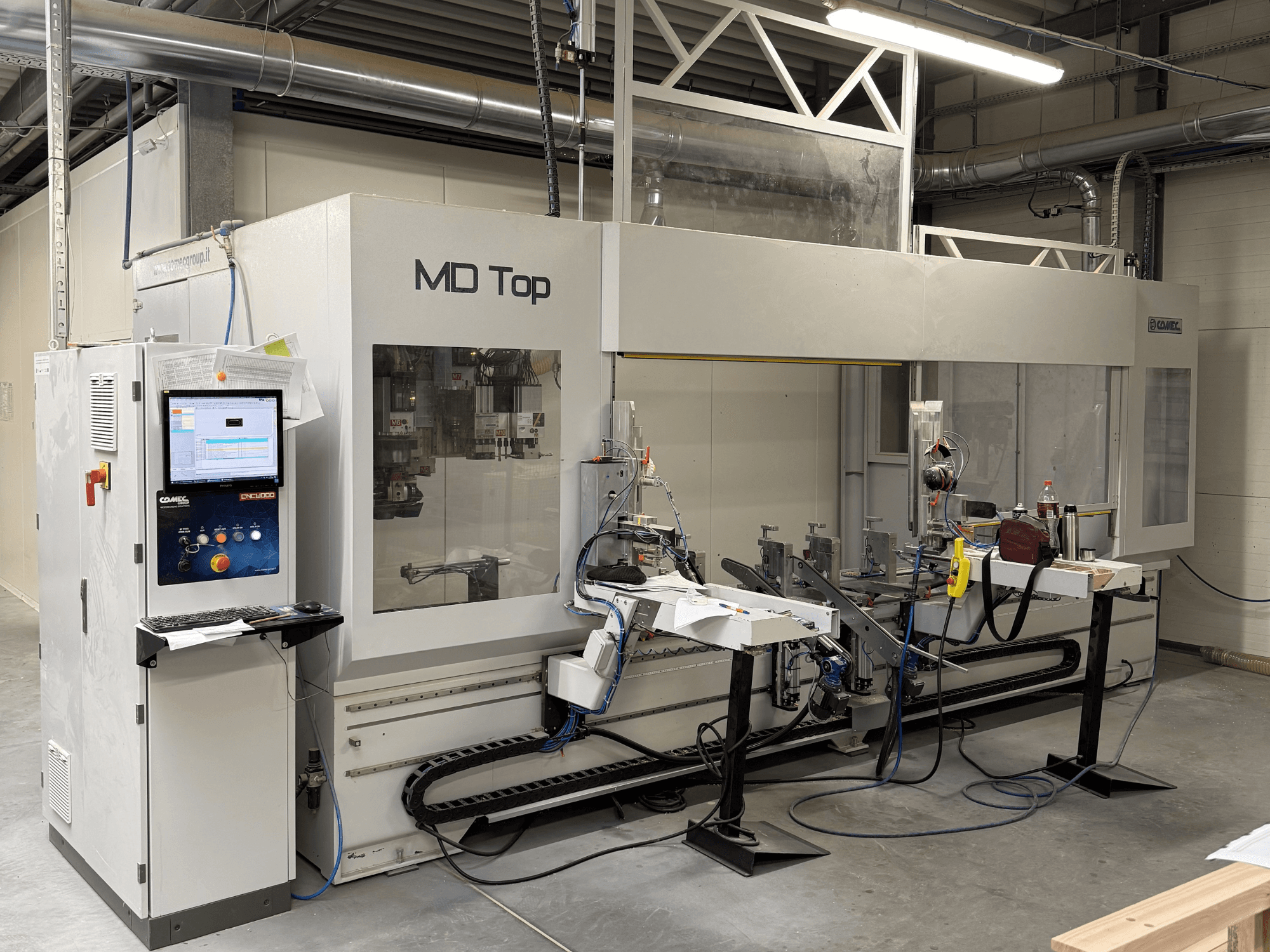 Máquina CNC MD Top vista de frente, con panel de control, brazos robóticos y espacio de trabajo con herramientas y materiales.