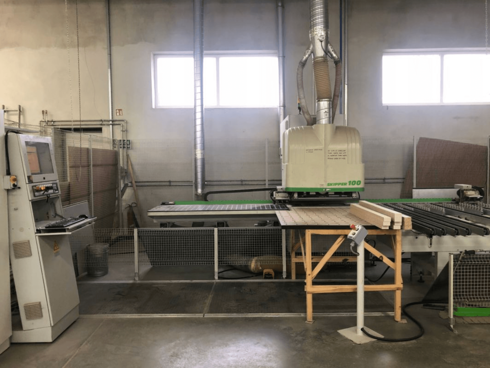 Centro de mecanizado CNC BIESSE SKIPPER 100 en un taller; la vista frontal muestra la máquina con el panel de control y la madera sobre la mesa.