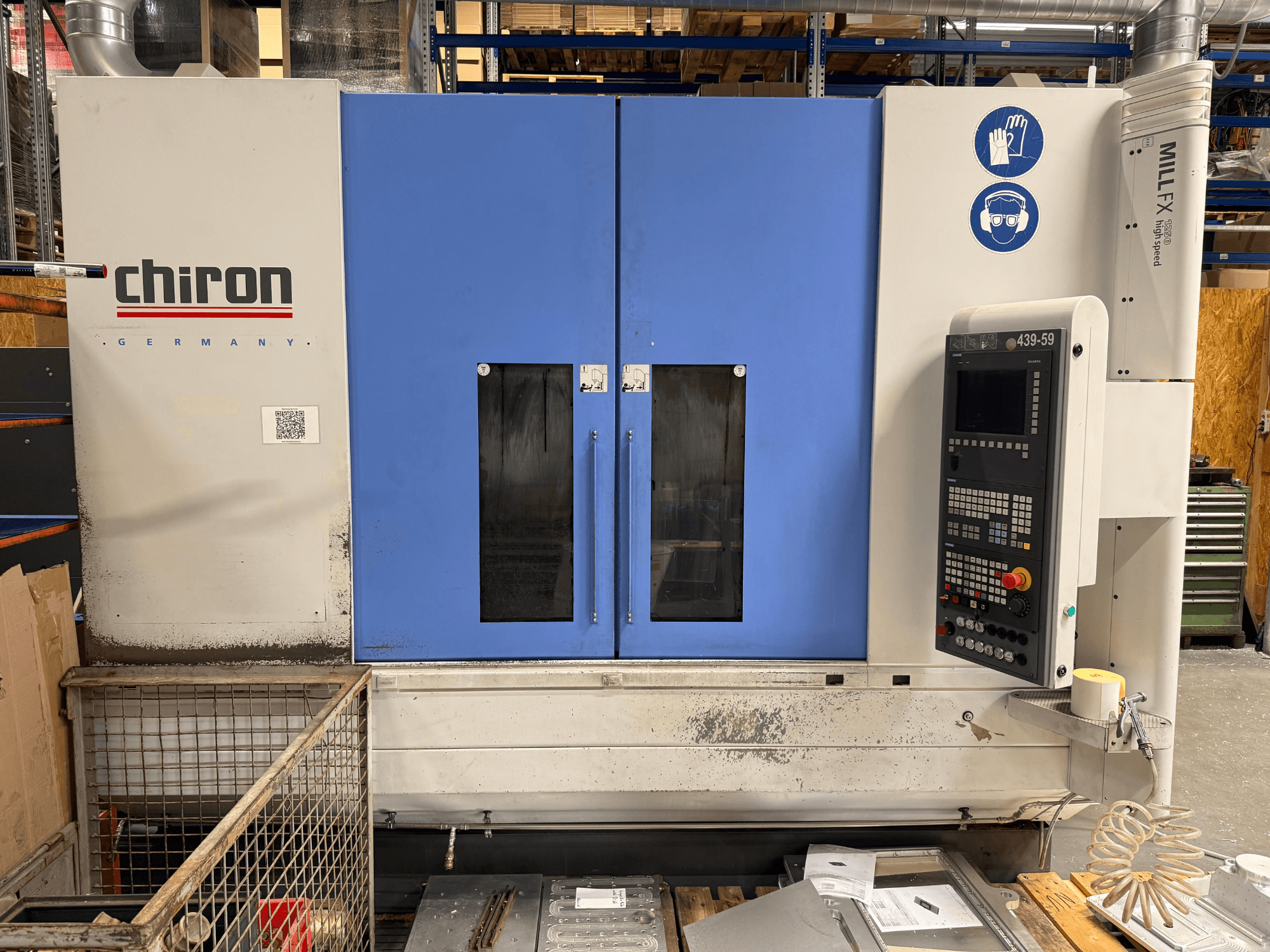 Centro de mecanizado vertical CHIRON MILL FX 1250, vista frontal, con el panel de control y los símbolos de seguridad, listo para trabajos de precisión.