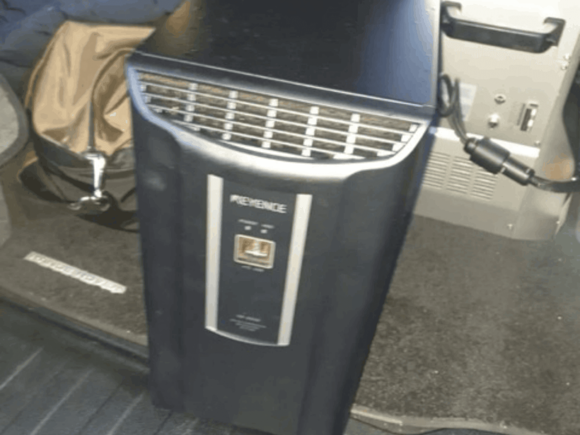 Sistema de automatización KEYENCE IM-8030 en una vista frontal, mostrando el panel de control y las rejillas de ventilación, sobre un fondo del interior del vehículo.