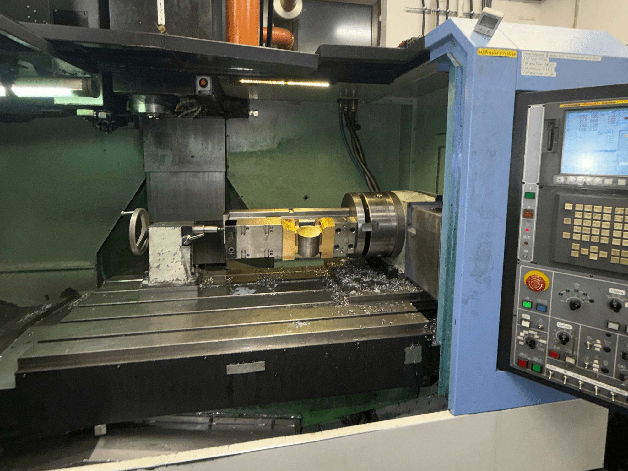 Centro de mecanizado vertical DOOSAN DNM650, vista frontal, en la que se aprecian la herramienta de corte y el panel de control, con virutas de metal visibles sobre la mesa.