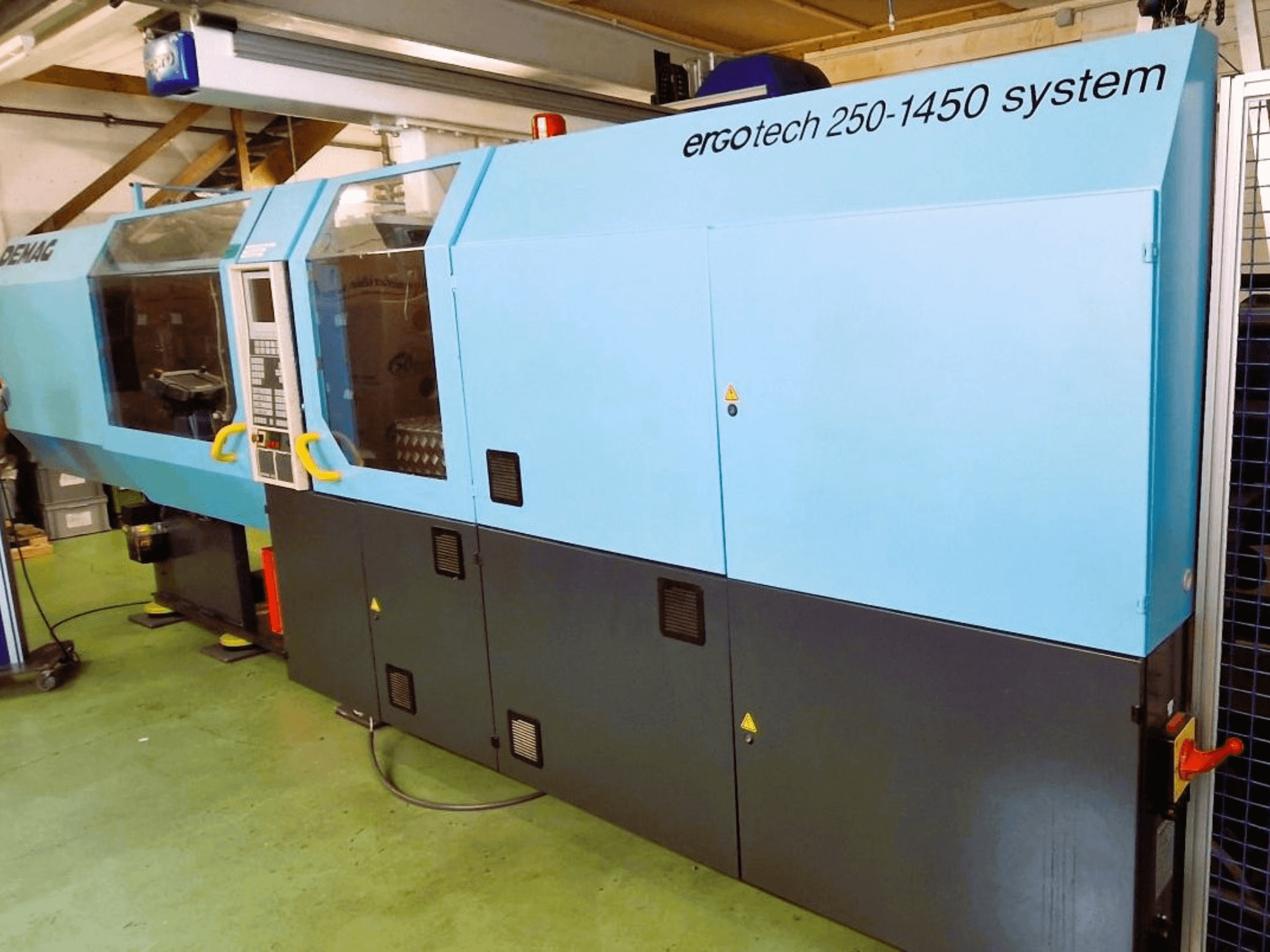 Máquina de moldeo por inyección de sistema Ergotech 250-1450, vista frontal, color azul y negro, con panel de control y elementos de seguridad visibles.