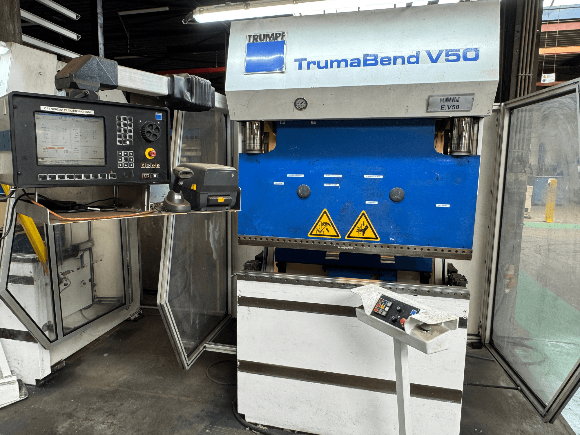Plegadora TRUMPF TrumaBend V50 desde una vista frontal, con panel de control, advertencias de seguridad y diseño distintivo en azul y blanco.