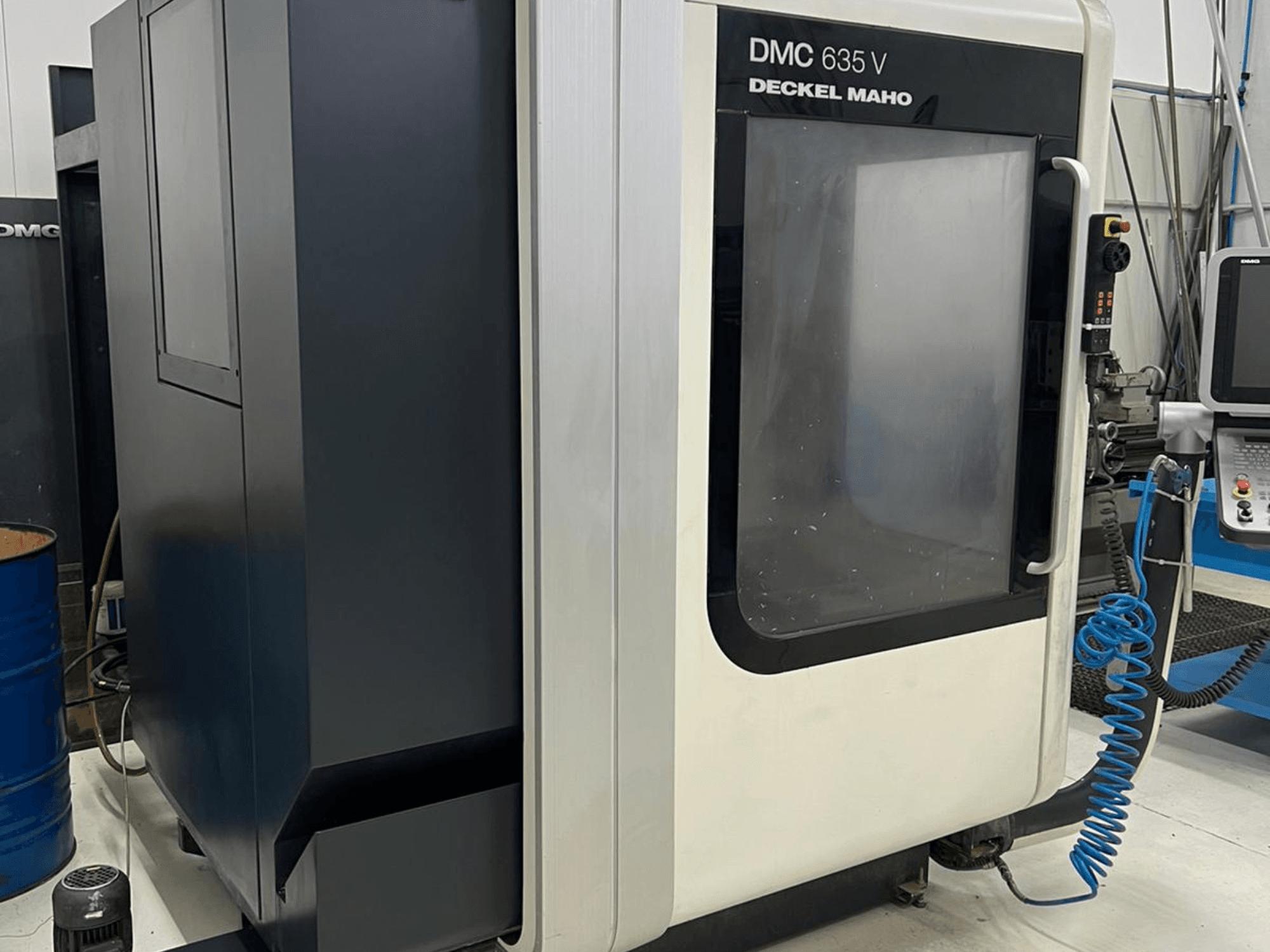 Fresadora DMC 635 V de Deckel Maho, vista lateral que muestra el panel de control y la puerta de acceso parcialmente abierta.