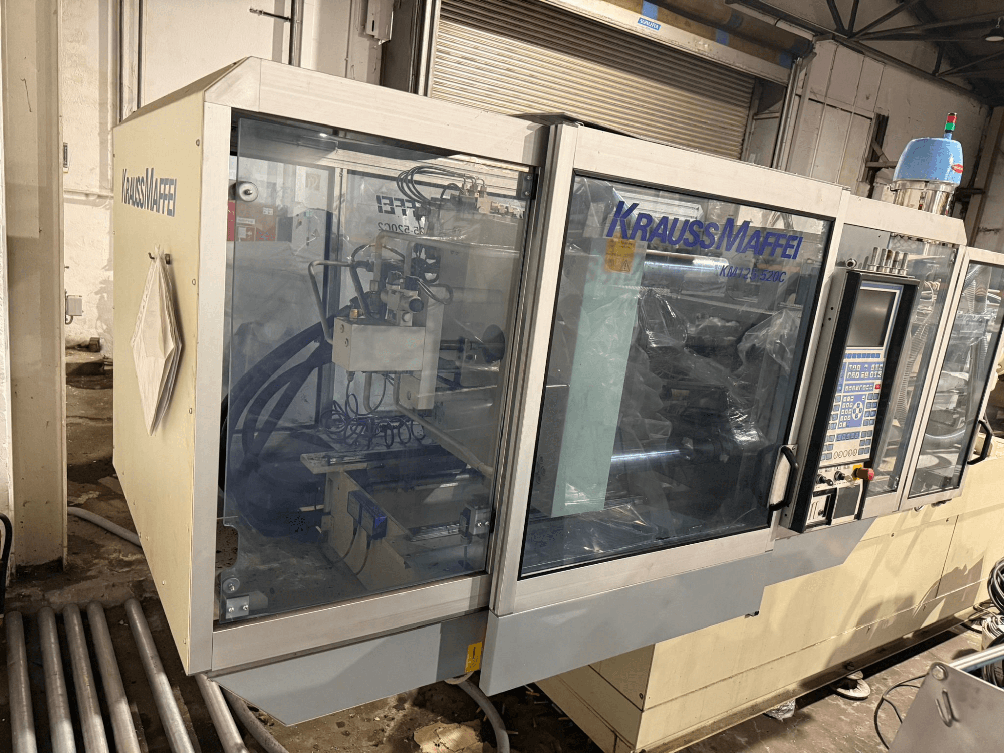 Máquina de moldeo por inyección hidráulica Krauss Maffei KM125-520C2, vista frontal con panel de control y carcasa transparente.